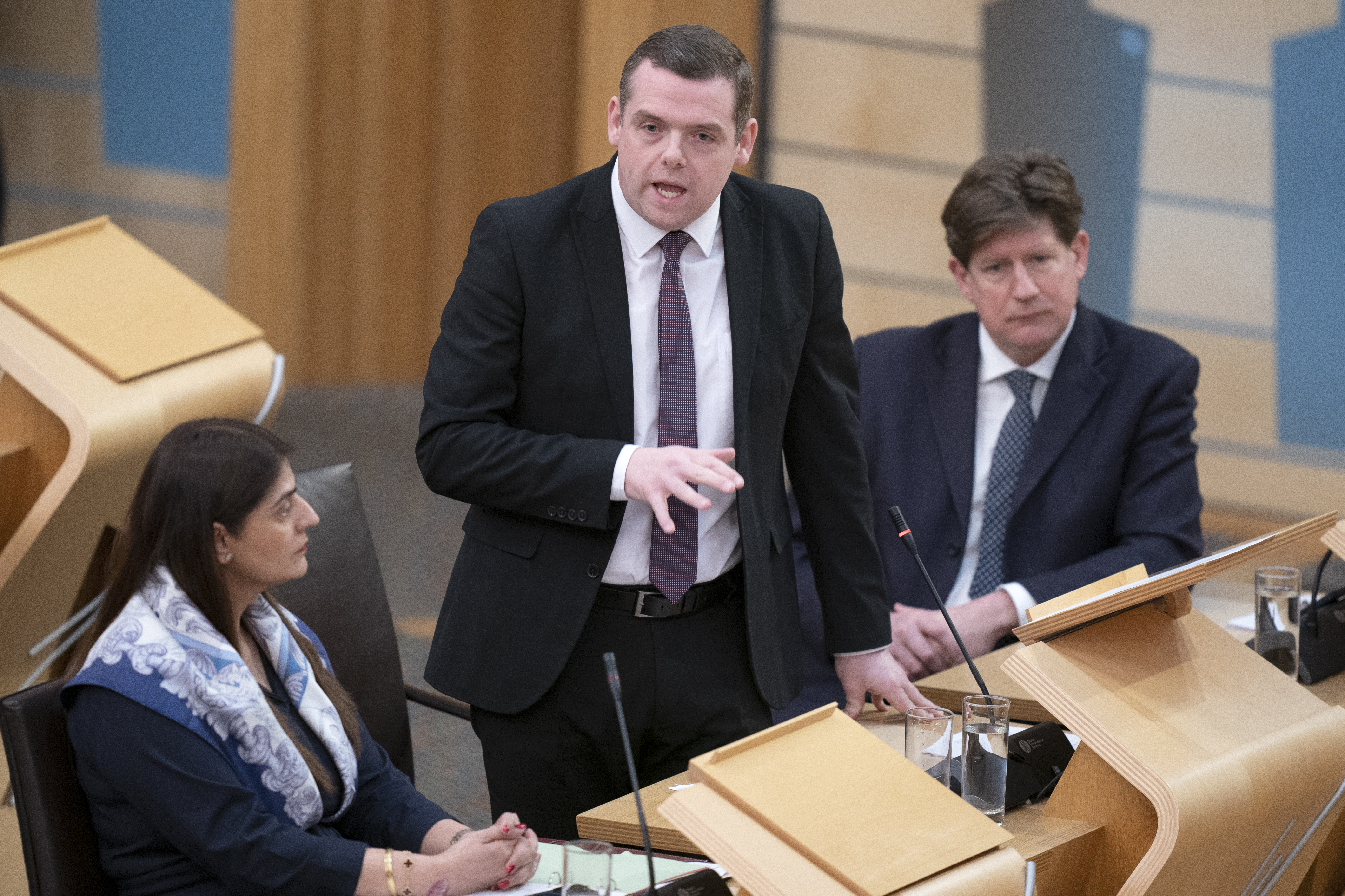 Douglas Ross standing while speaking in Holyrood's debating chamber, with Tory MSPs on either side of him