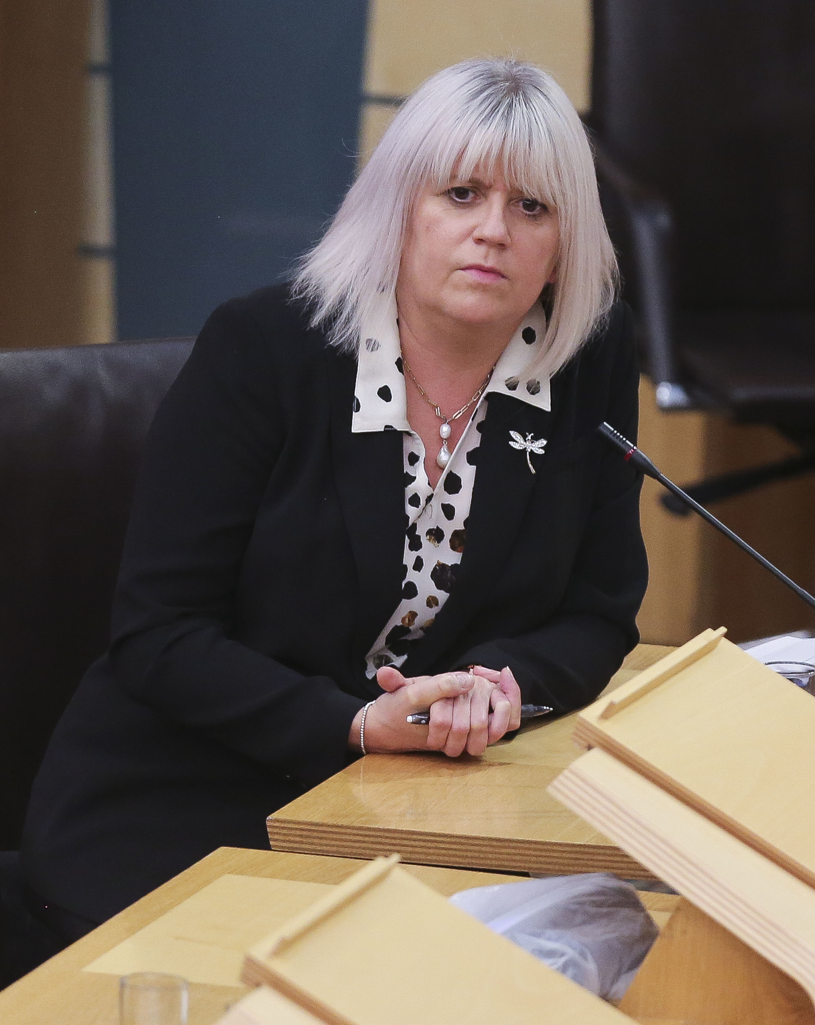 Sue Webber seated at a desk in the Holyrood debating chamber, with her hands clasped together