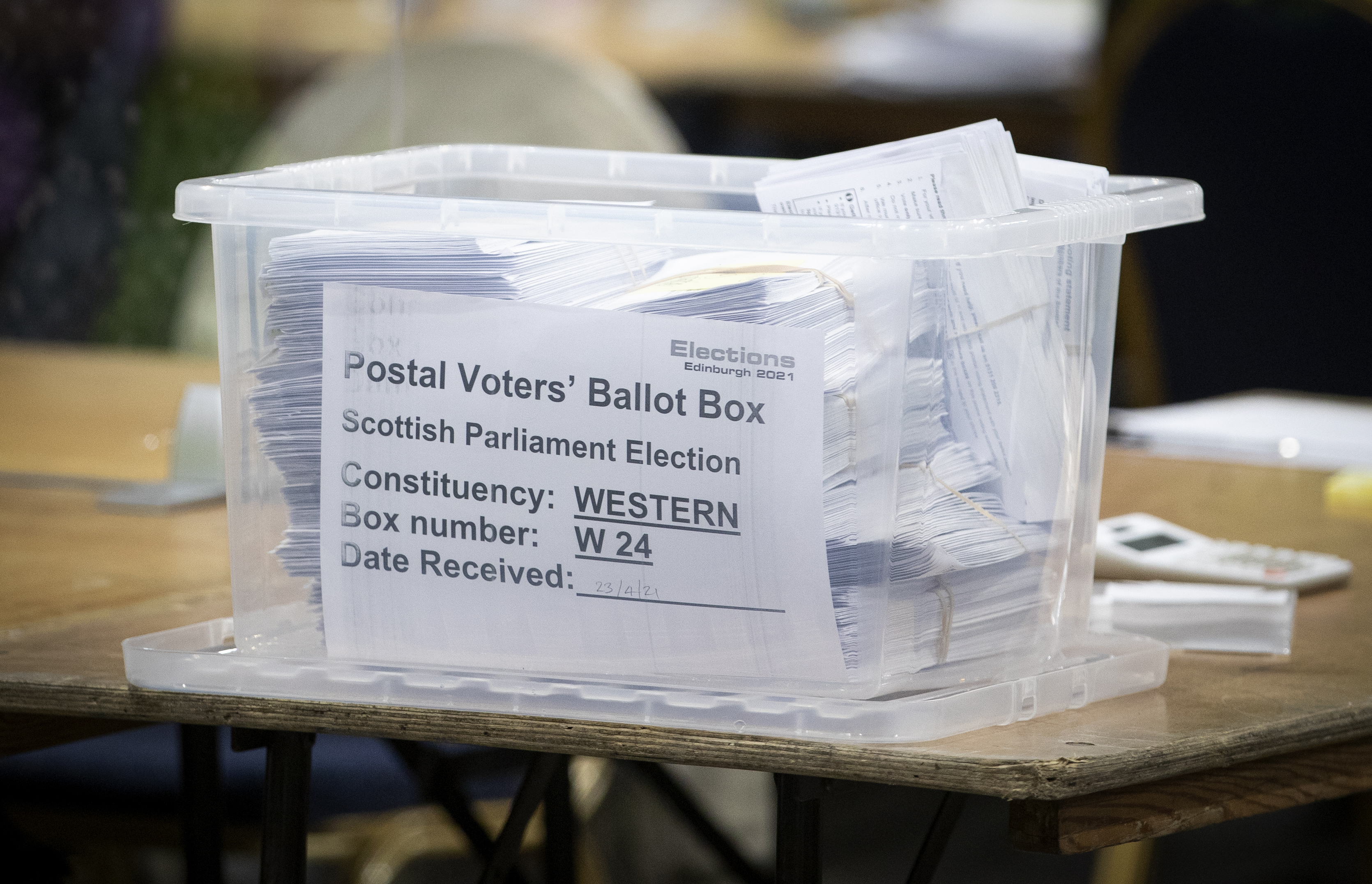 A large plastic box filled with ballot papers , with a label reading 'postal voters' ballot box' on the front