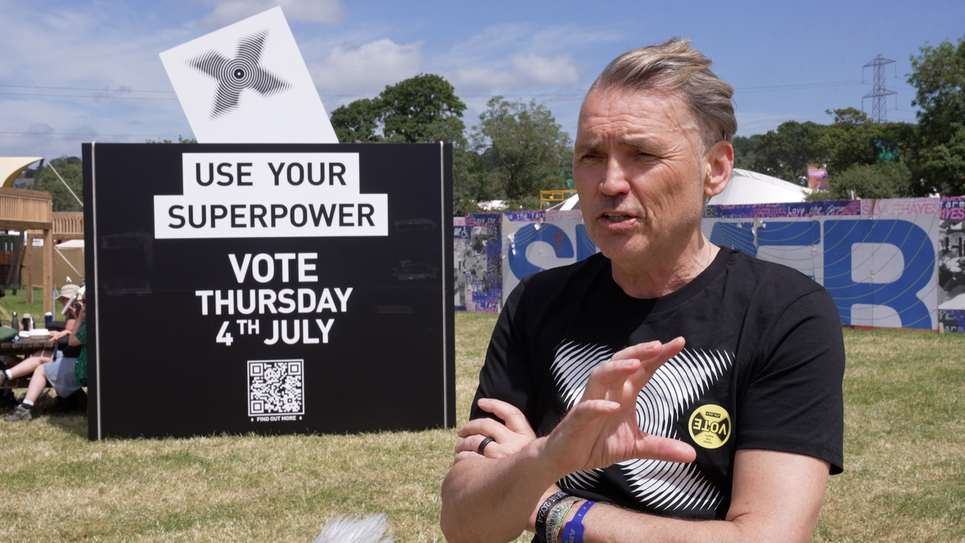 Ecotricity's Dale Vince speaks in front of a black giant ballot box at Glastonbury which features the message 'Use Your Superpower. Vote Thursday 4th July'