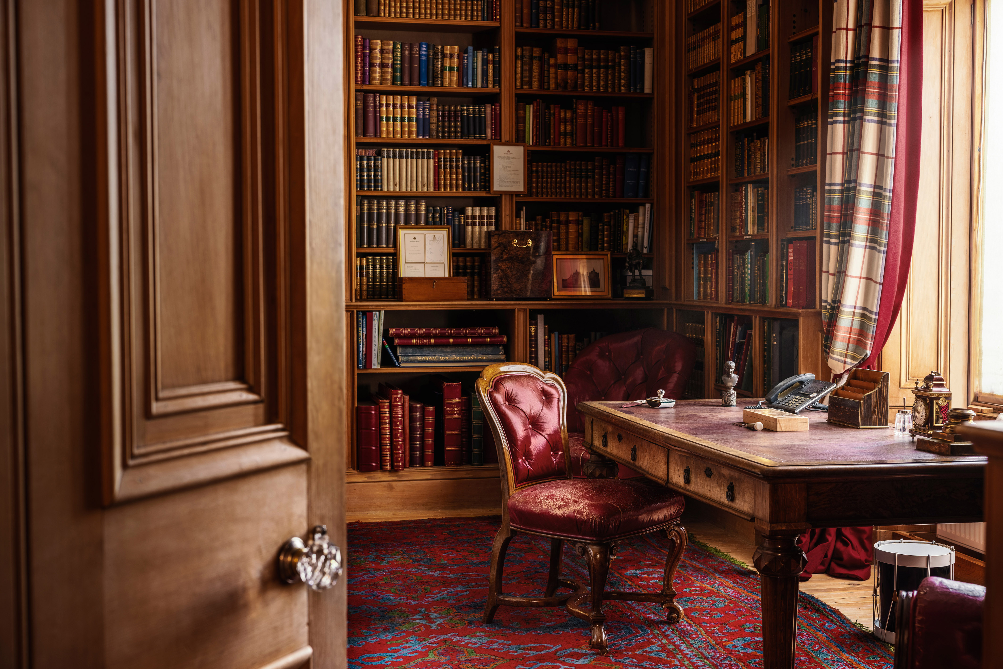 An open door reveals a chair at a desk with books on shelves in Balmoral's library