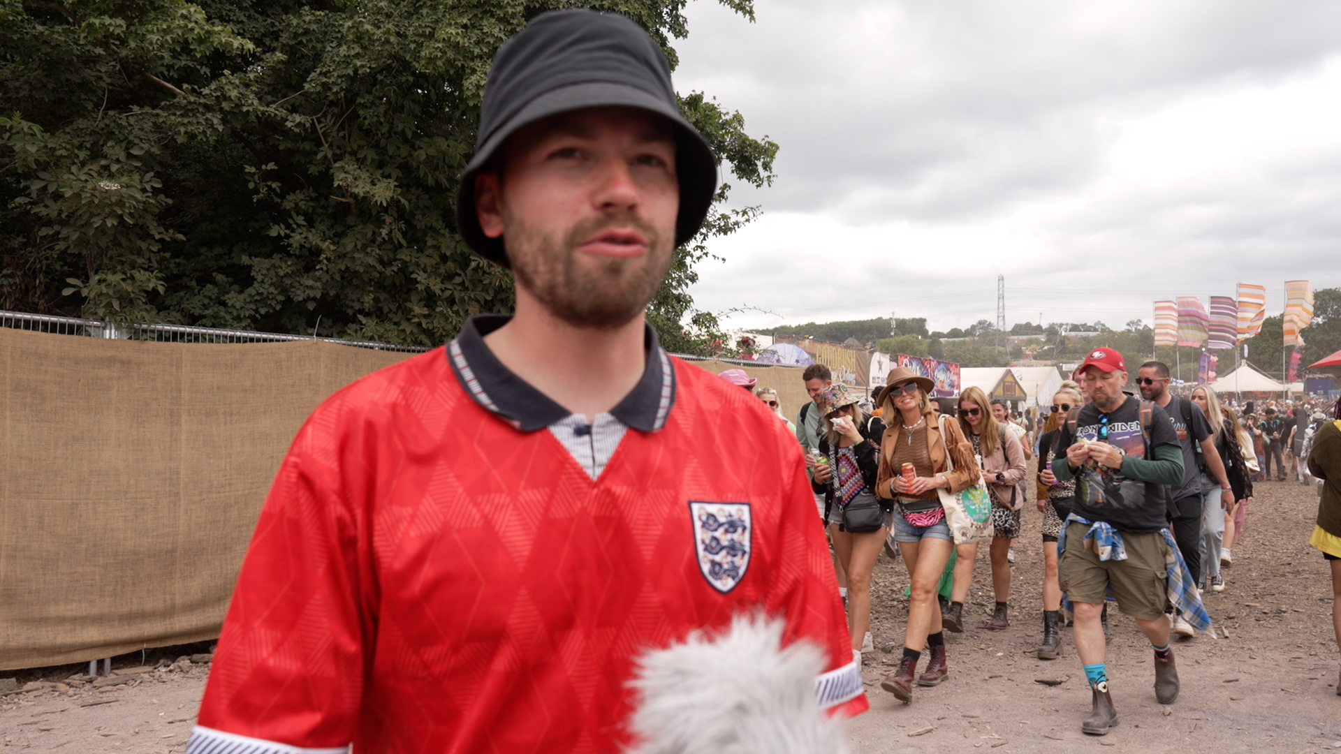 Alistair Tomlinson wearing a red England shirt and a black bucket hat at Glastonbury 