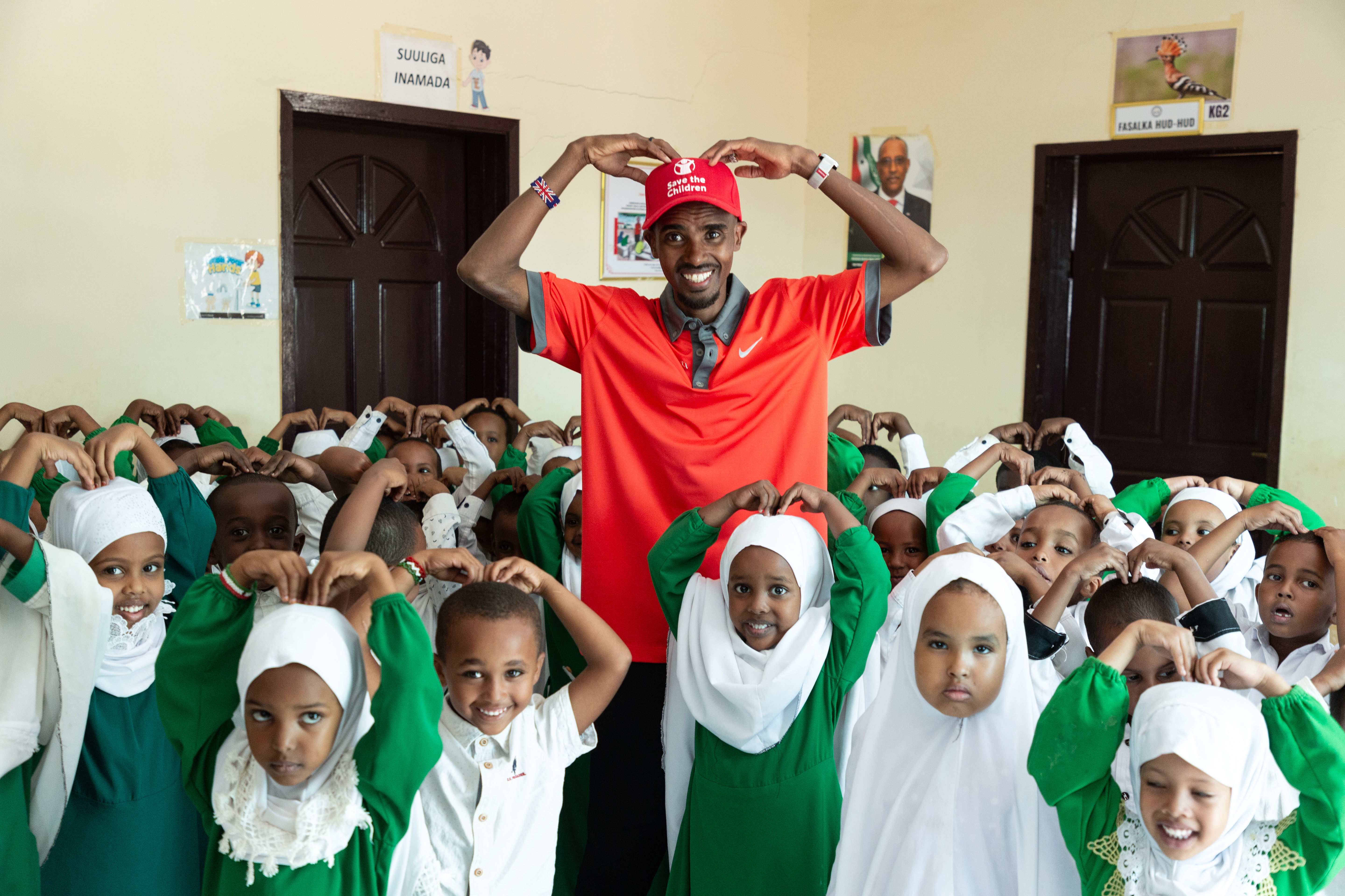 Sir Mo Farah, wearing a re Save the Children cap, does the Mobot pose with schoolchildren dressed in green and white in Somaliland