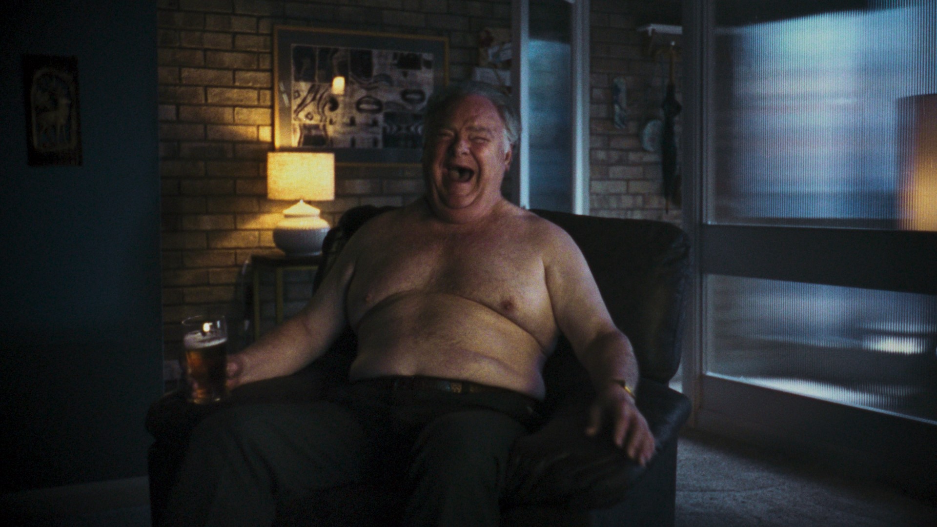 A fat man sitting in a chair in his living room with his top off