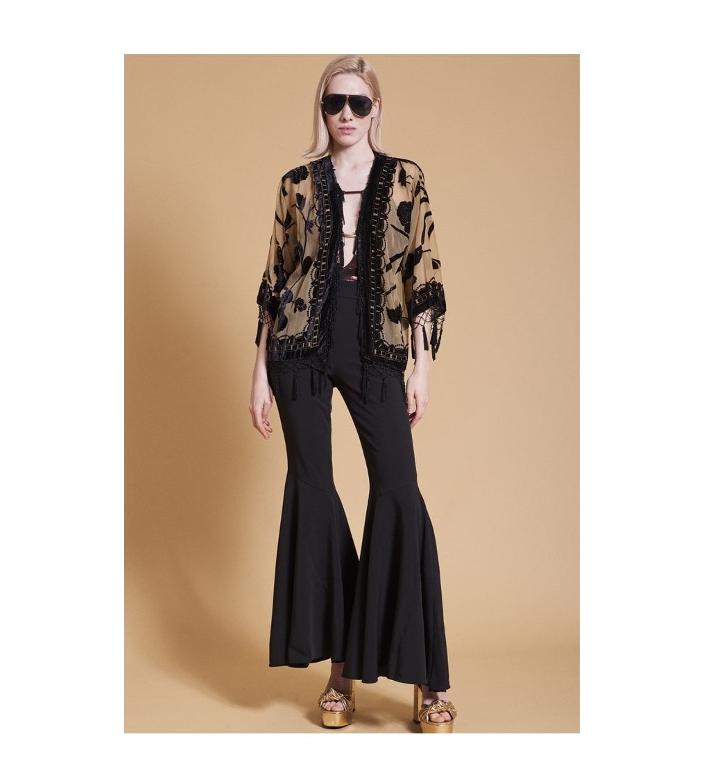 Woman wears beige and black embroided tassle shawl with black flared trousers and aviator glasses and glod block heels