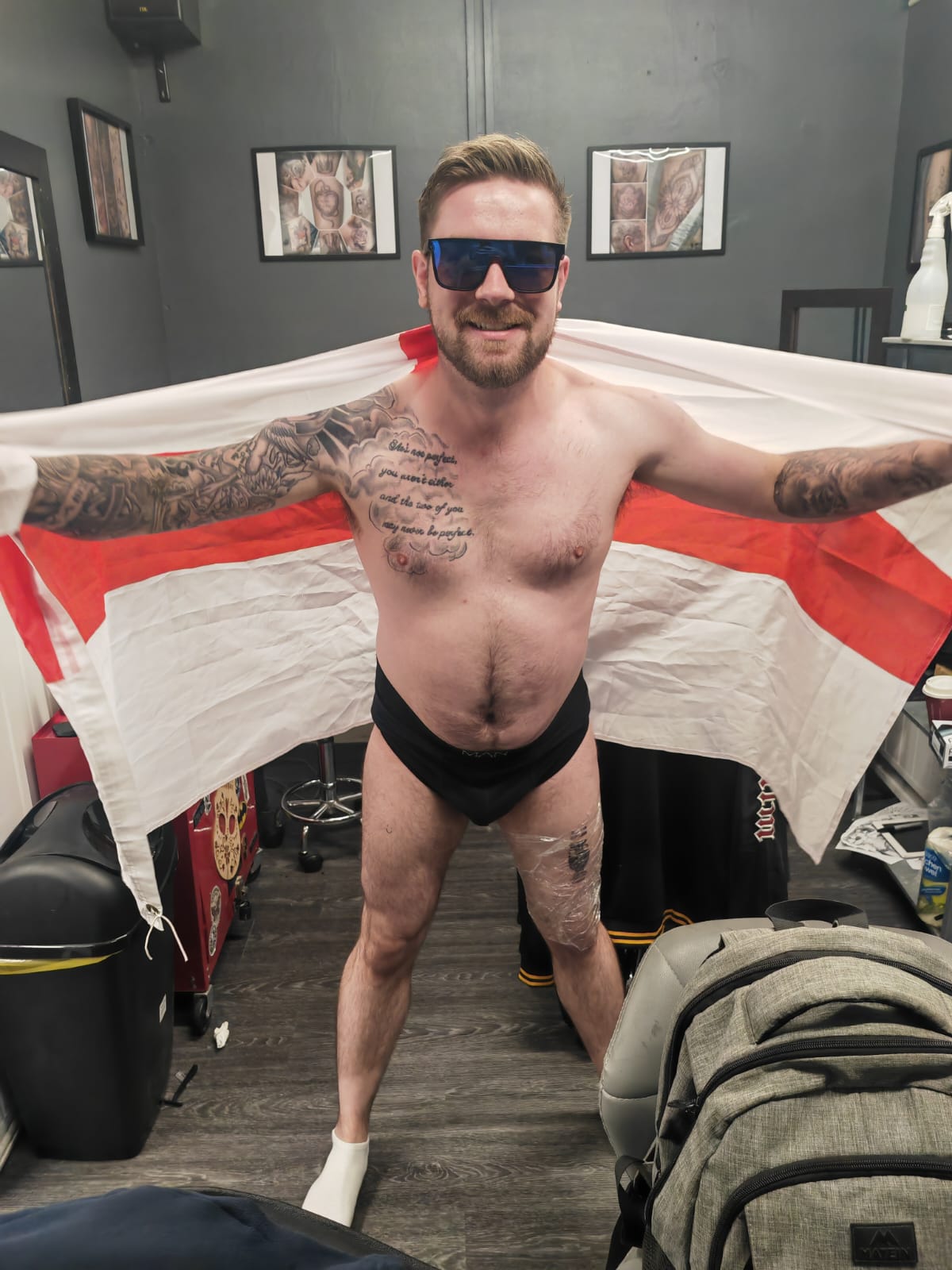 Man wearing just his boxers and sunglasses while holding a England flag after his tattoo