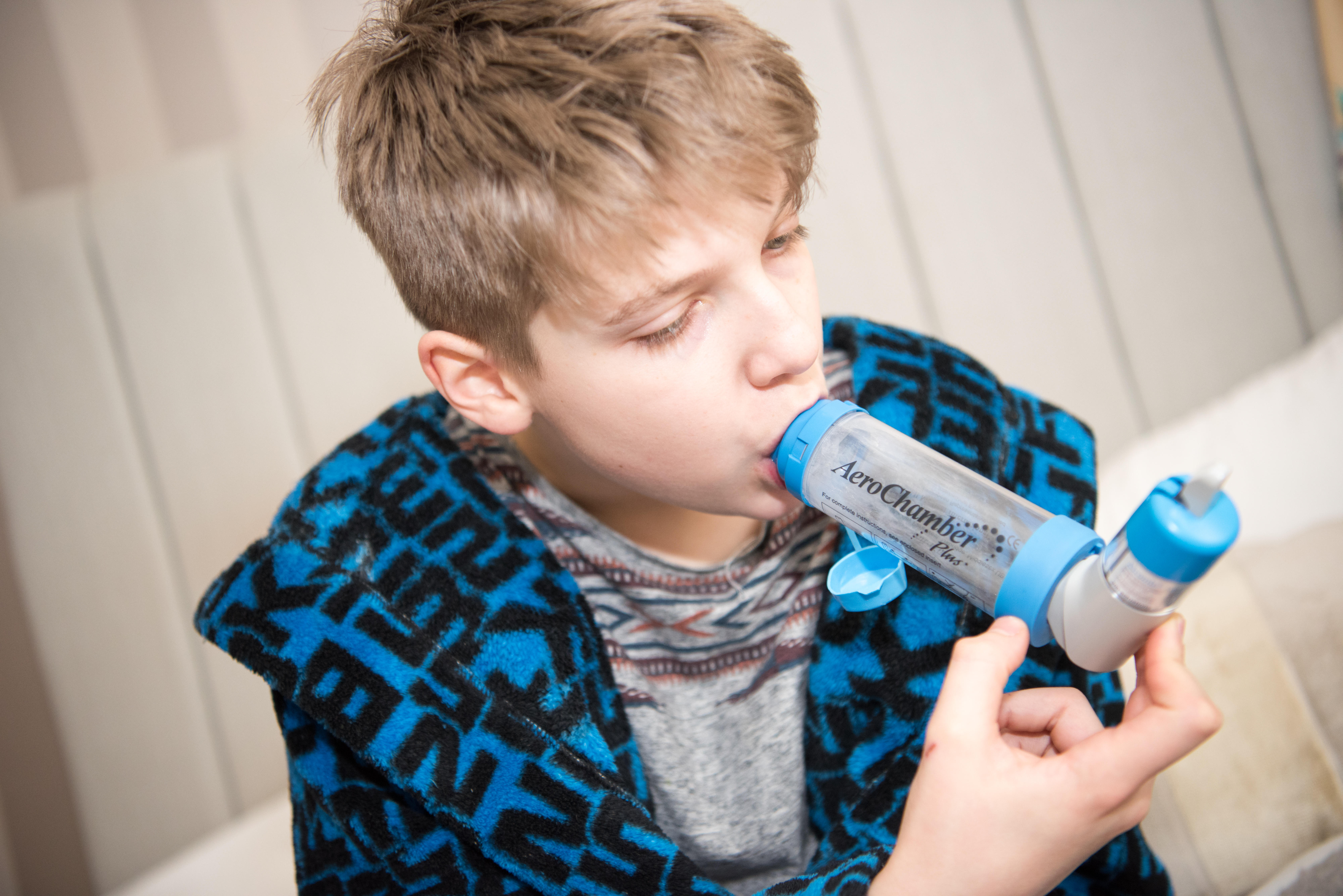 Poorly teenage boy suffering a dangerous asthma attack taking breaths through a spacer and his inhaler to get ventolin to help him breathe