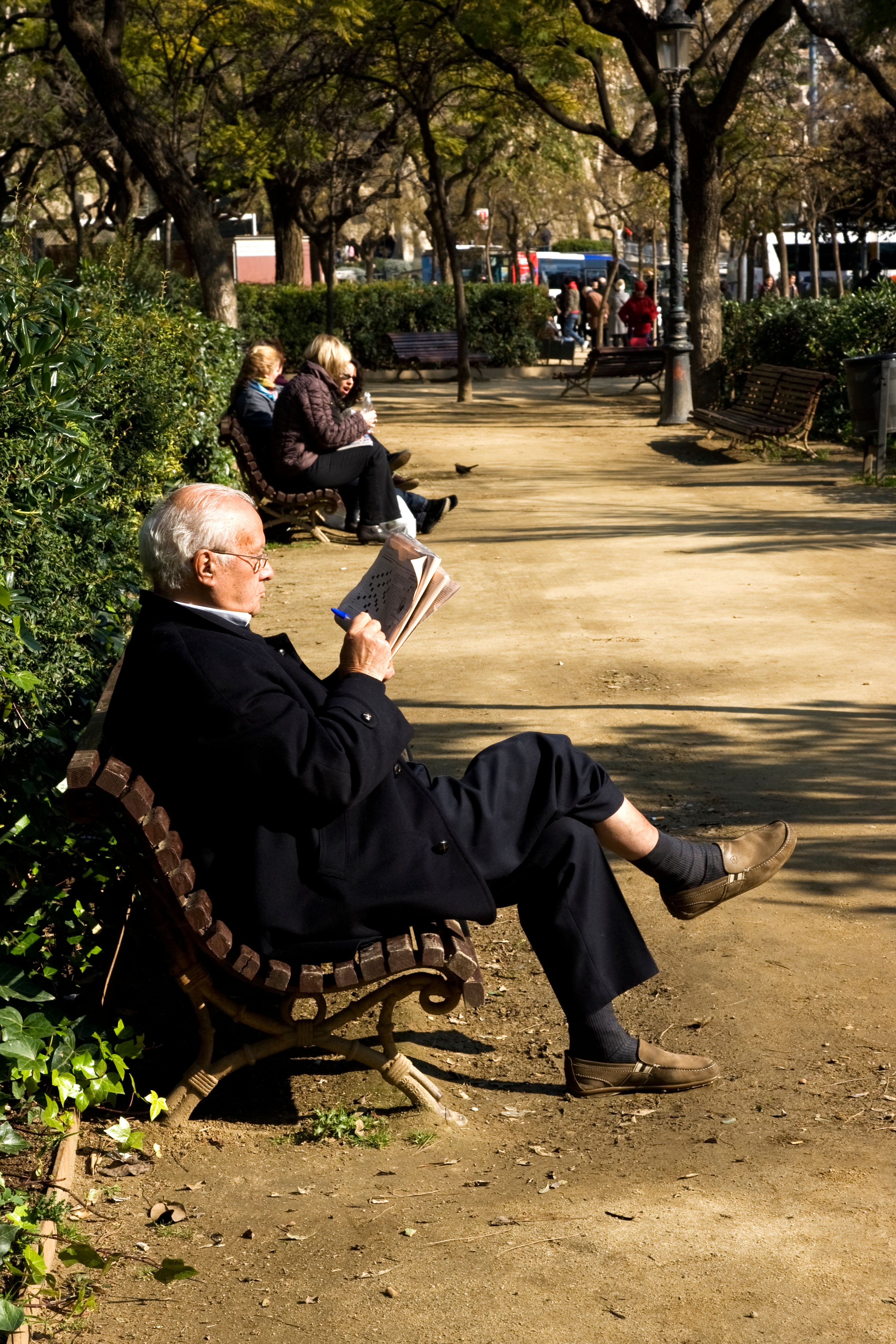 Well dressed older man sitting on a park bench doing the crossword of a newspaper