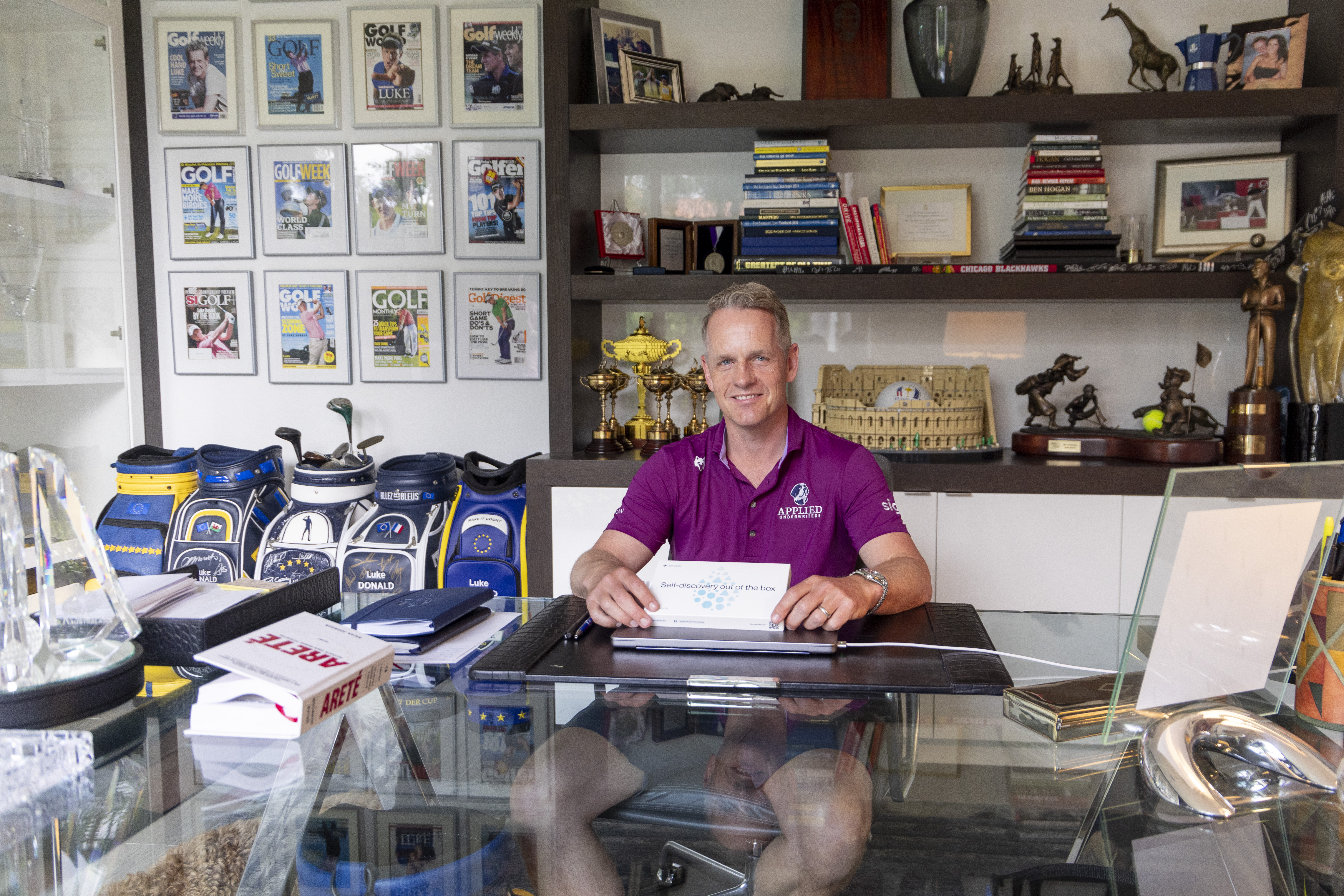 Luke Donald sits behind a glass-topped desk surrounded by golf memorabilia