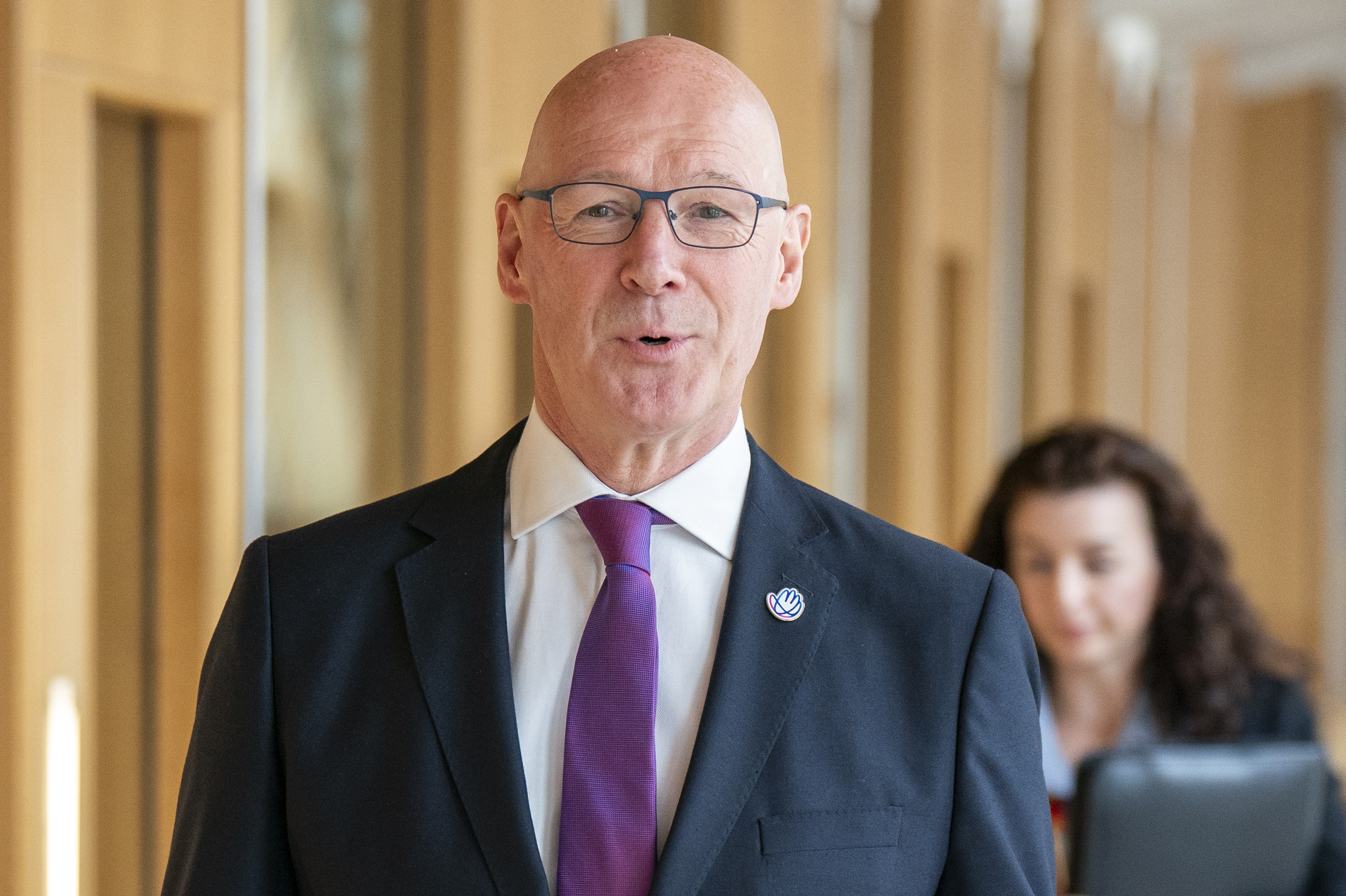 John Swinney smiles at the camera as he walks to First Minister's Questions