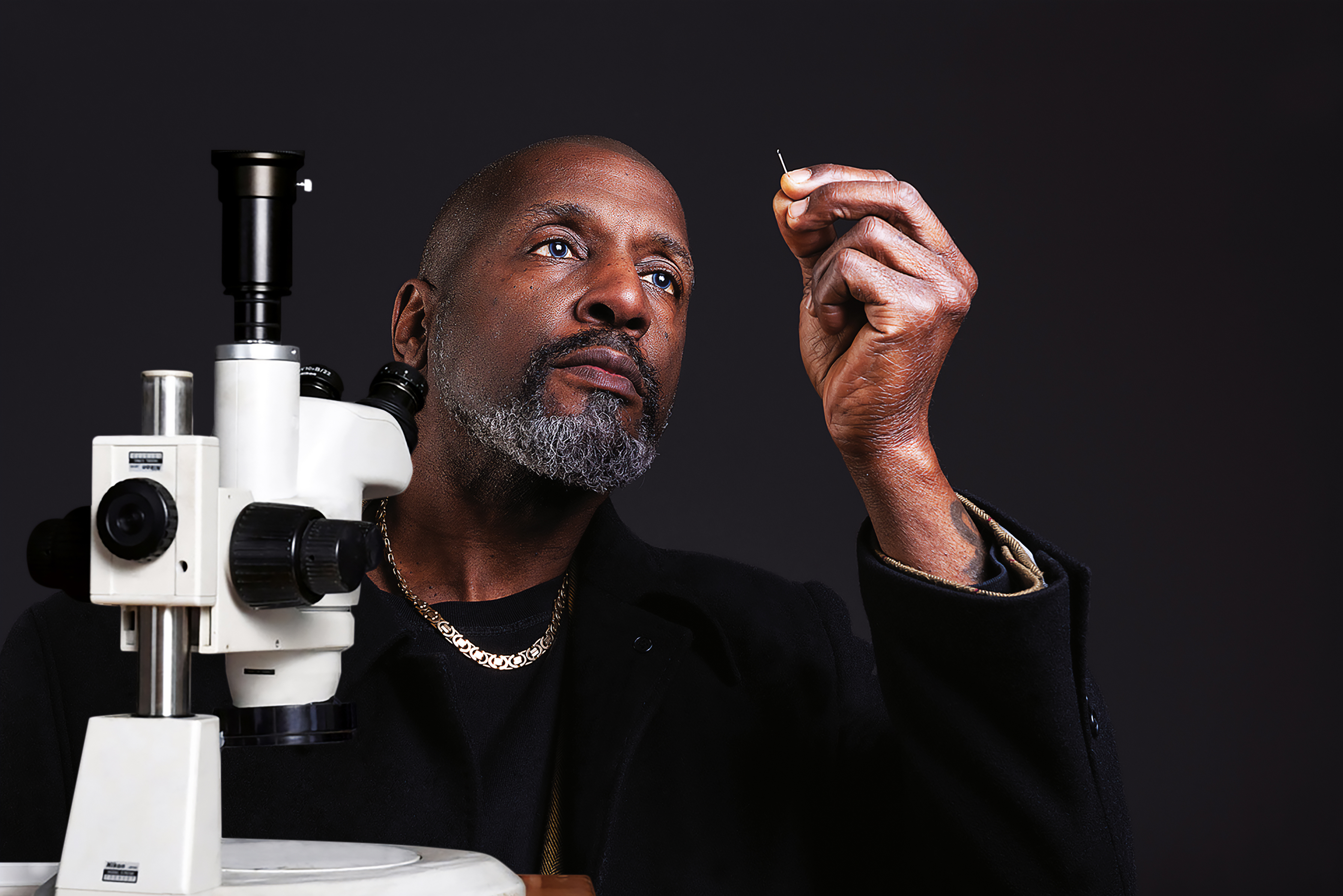 Dr Willard Wigan looking through the eye of a needle while a microscope sits beside him