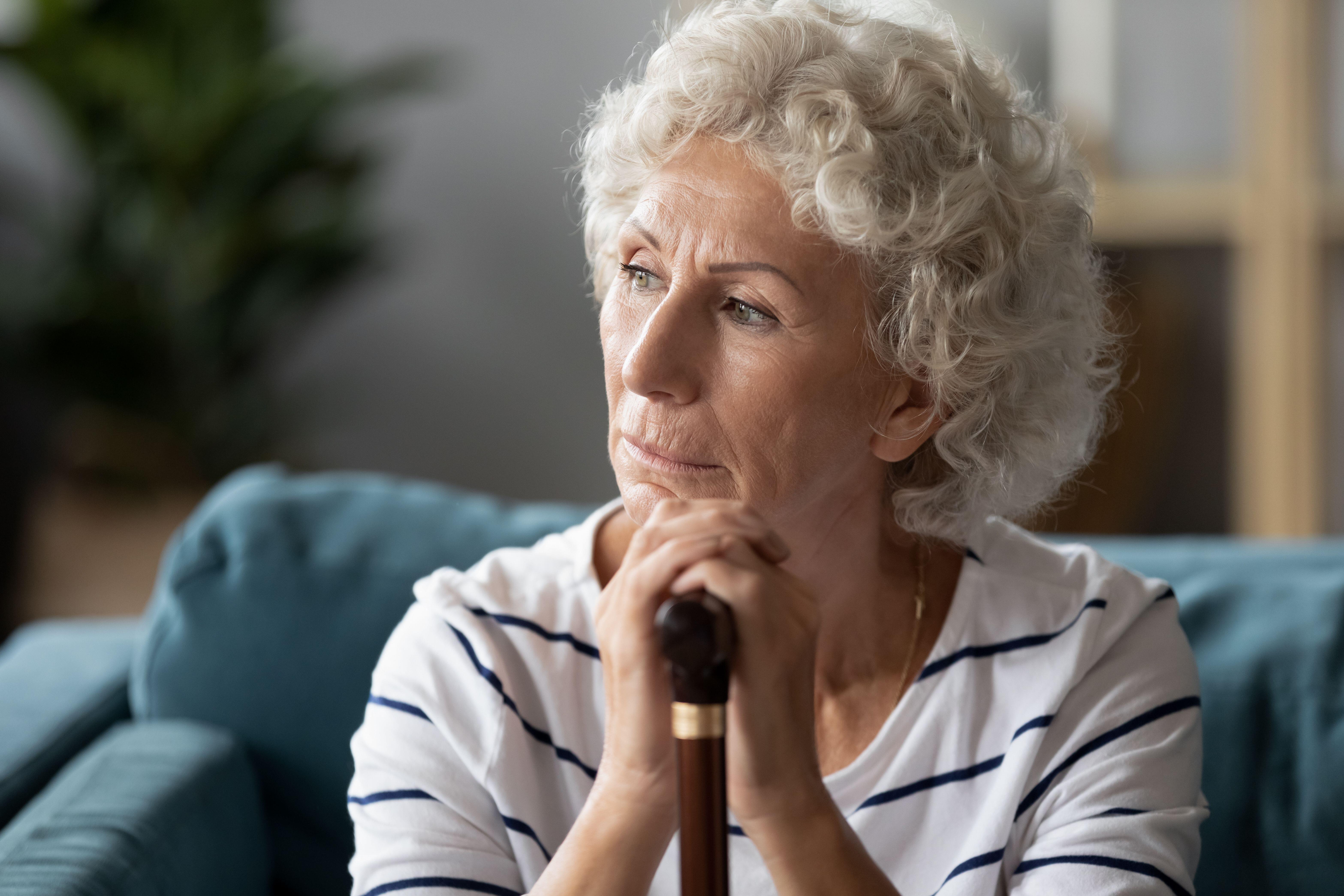 Old woman sit on sofa holding cane looking away