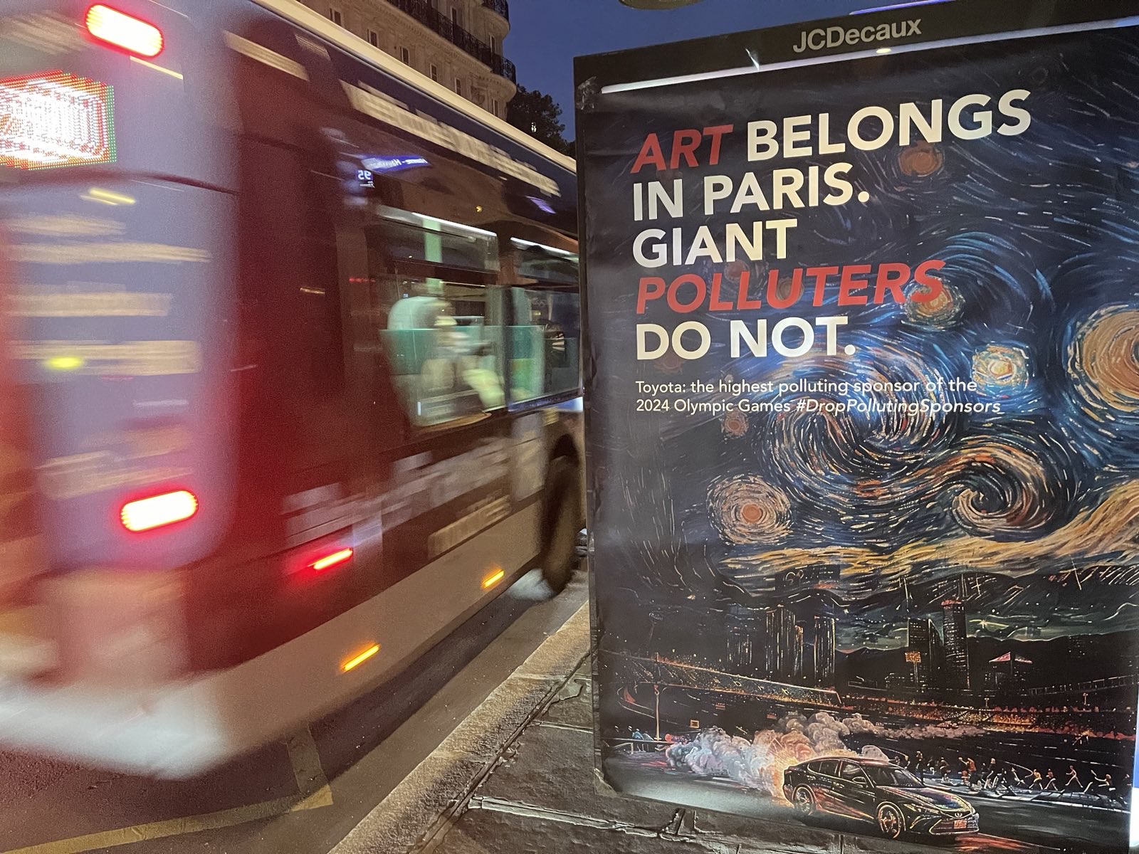 A protest poster with the words Art belongs in Paris. Giant polluters do not, and a passing bus blurred out