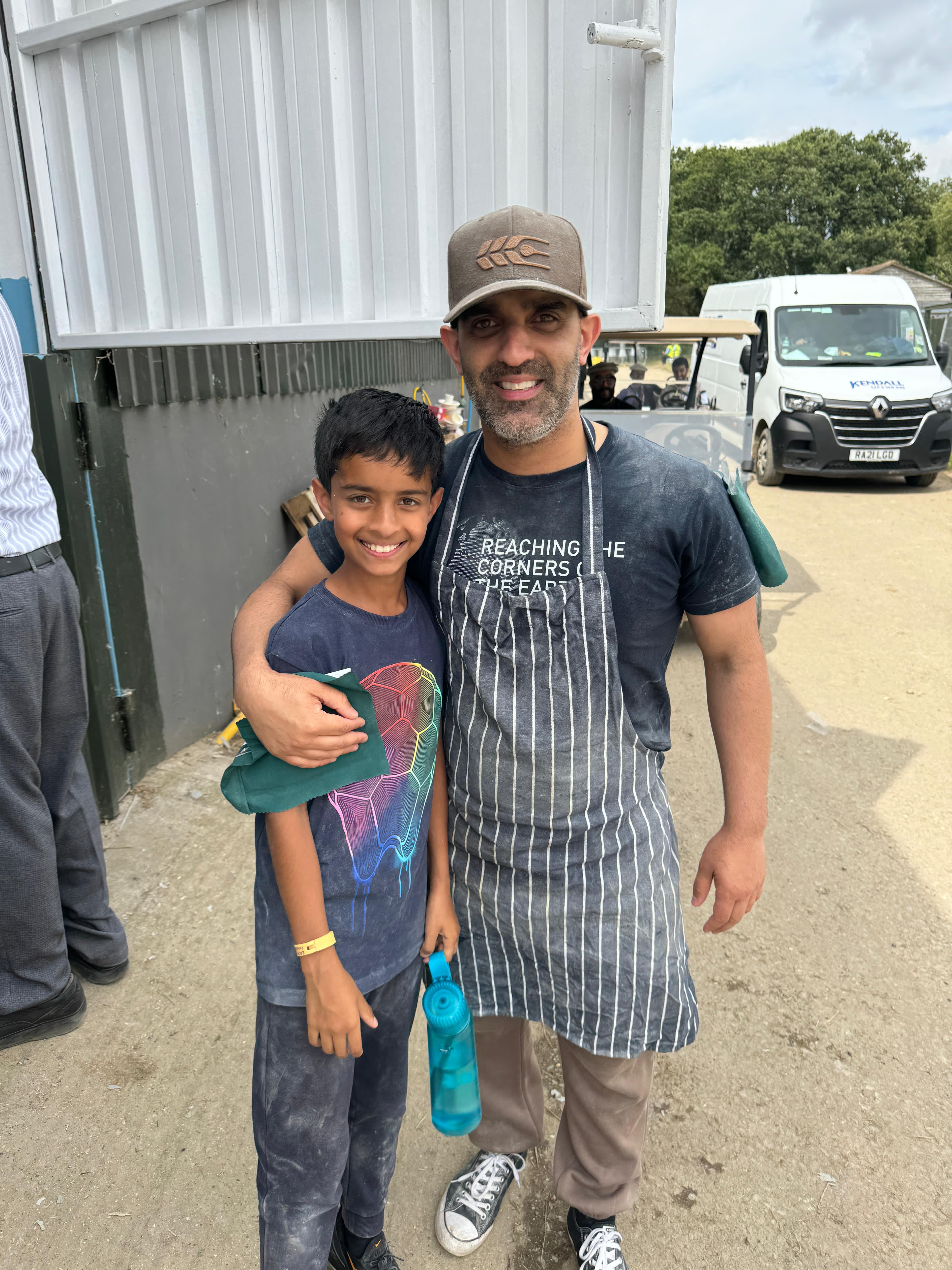 Faraz Sethi standing with his arm around his son, Zachariah Sethi, outside the on-site roti plant at the Jalsa Salana 