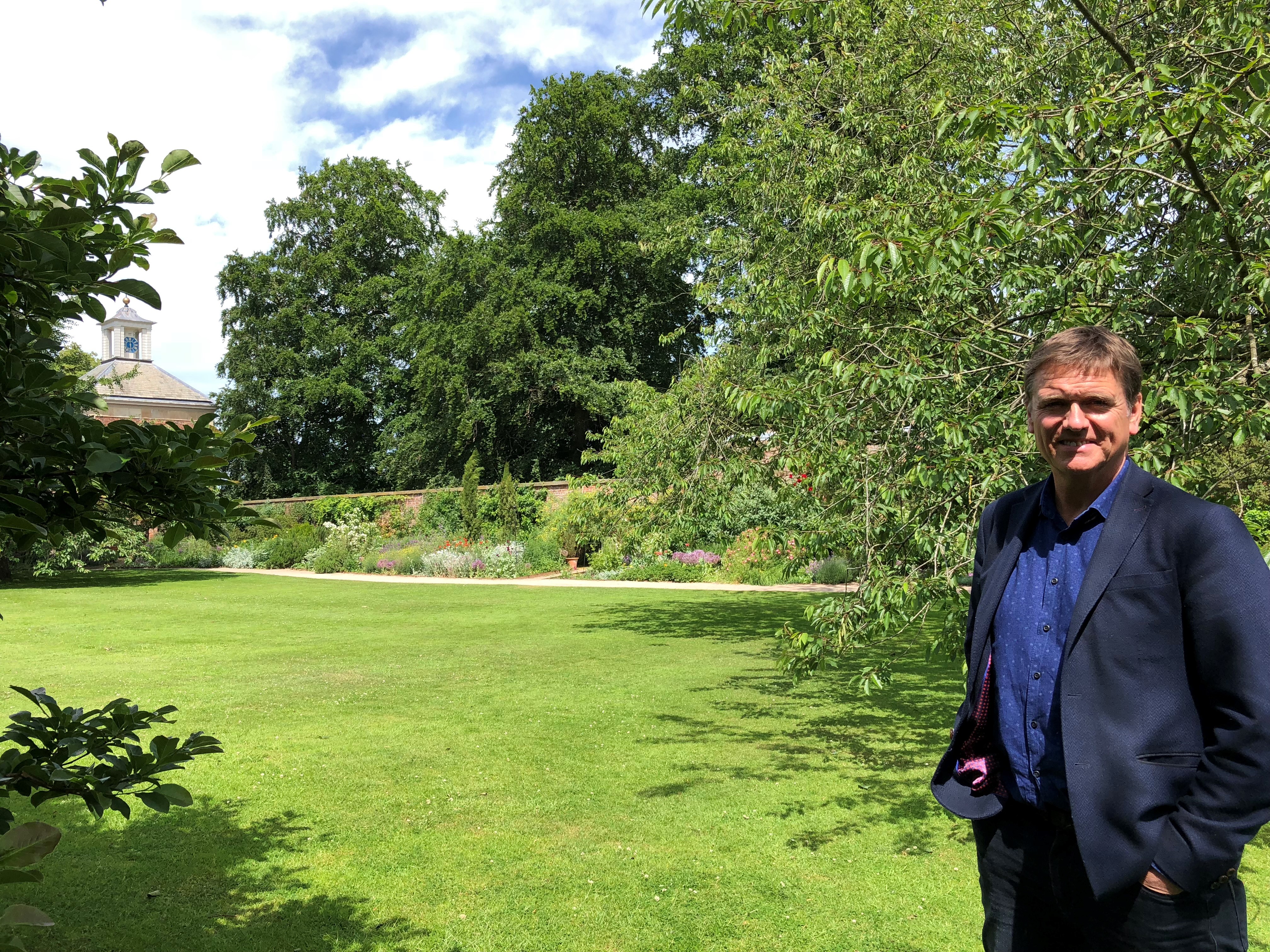 Garden designer Andy Sturgeon stands in front of an area of lawn with a herbaceous border behind