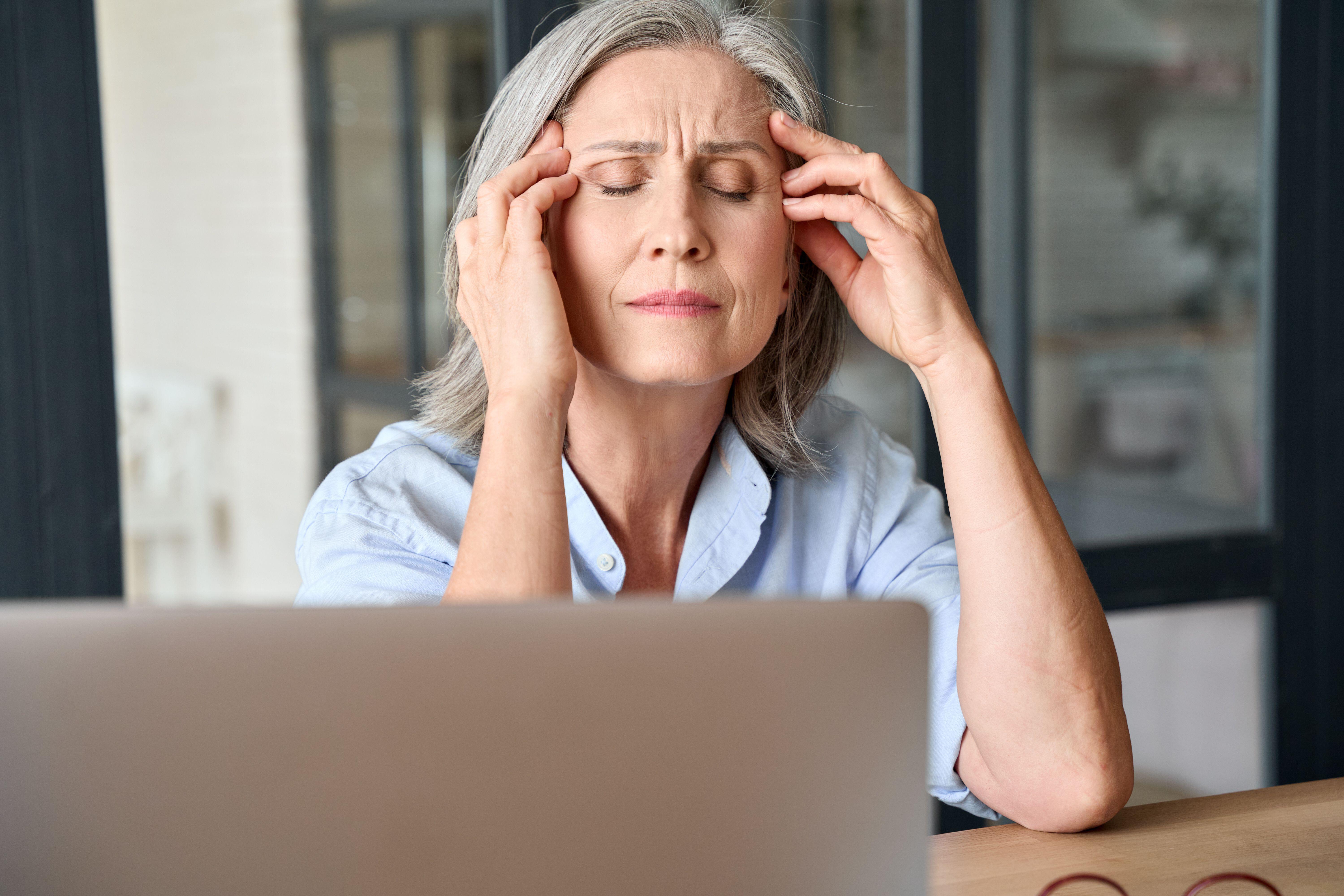 Senior woman with grey hair looking stressed and massaging her head 