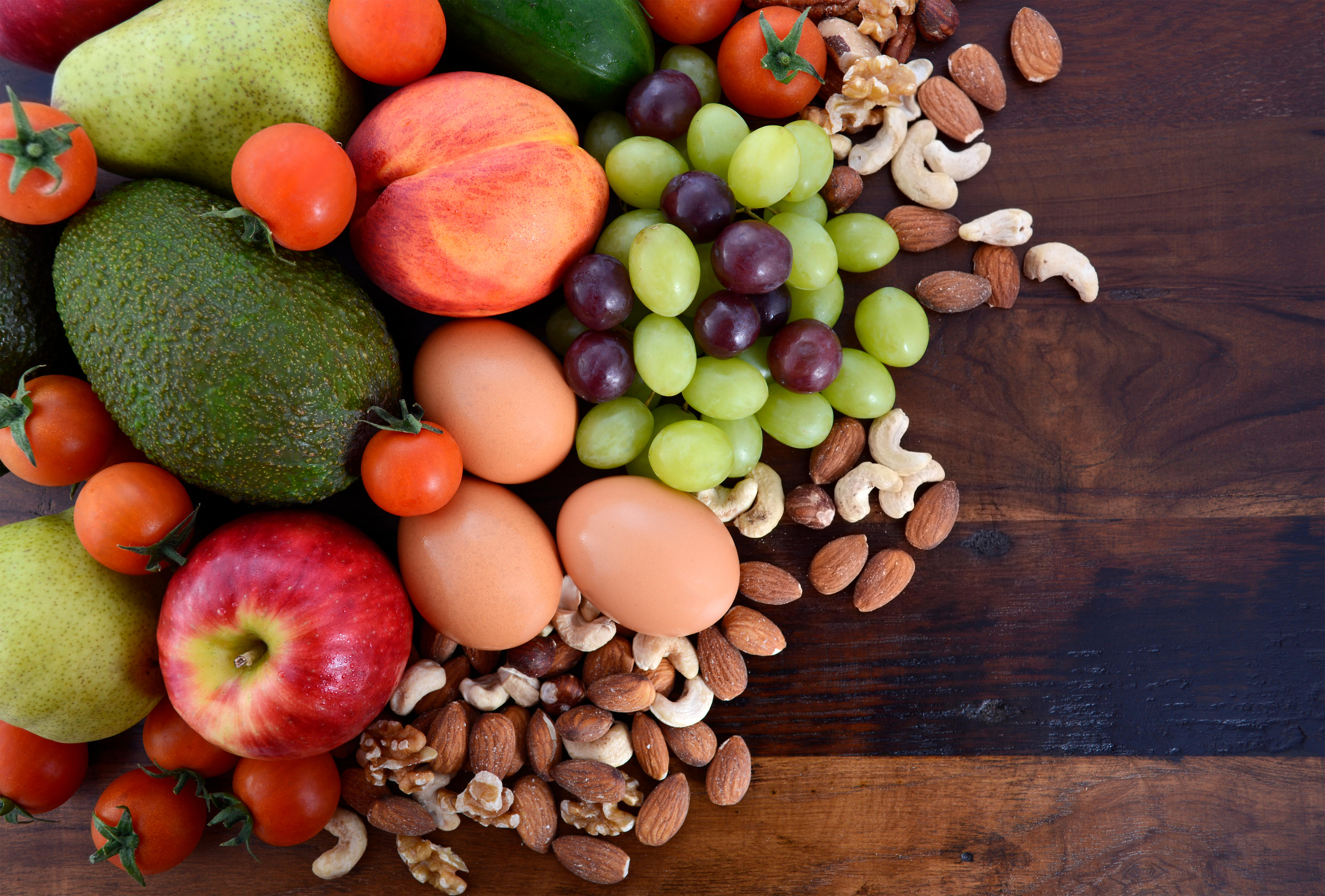 Fresh fruit, apples, pears, avocados, grapes, eggs, nuts, tomatoes cucumbers on a rustic wood background.