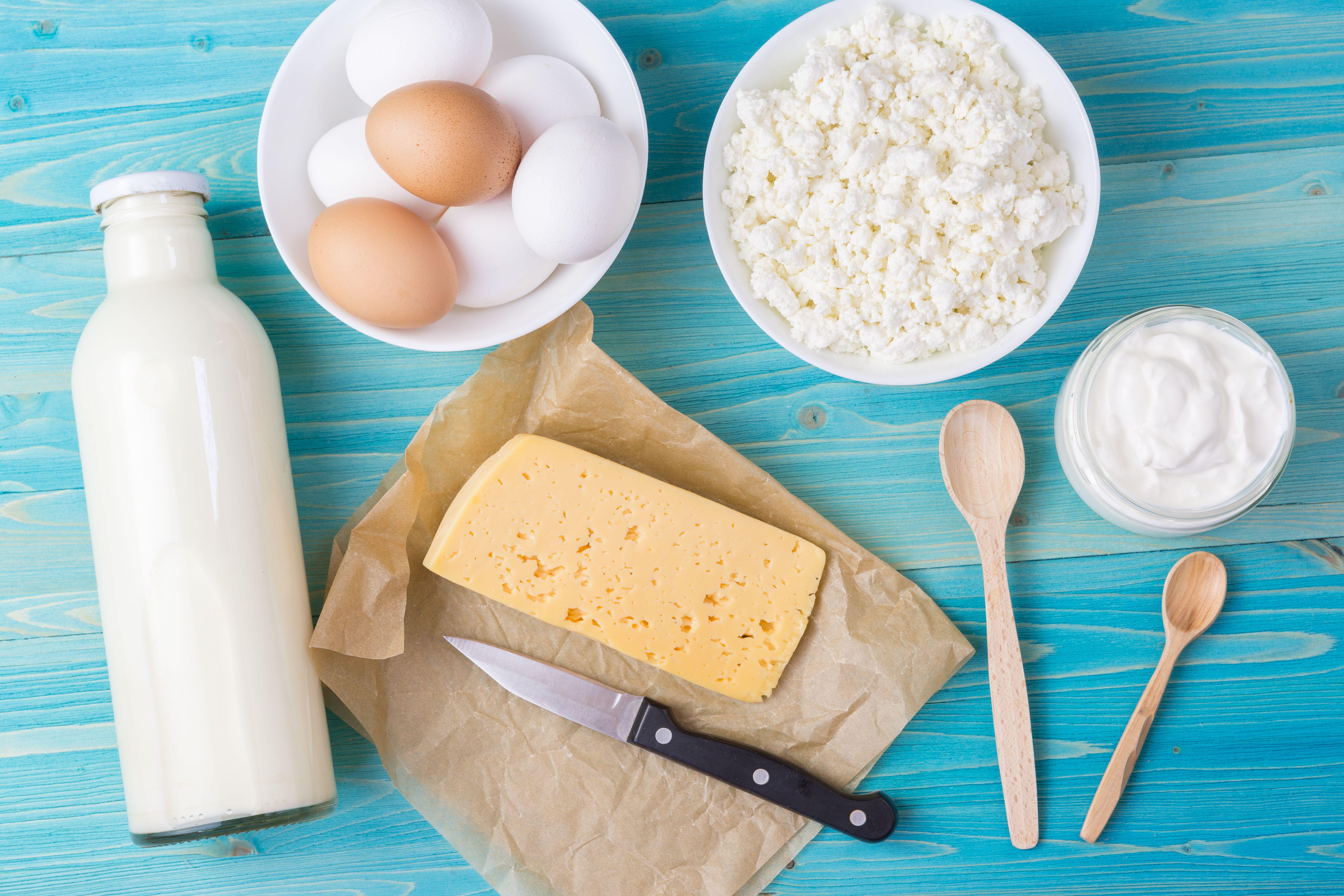 Fresh milk, cottage cheese, sour cream and cheese on paper, as well as eggs in a bowl lie on a blue wooden table. Natural and healthy, calcium-rich food