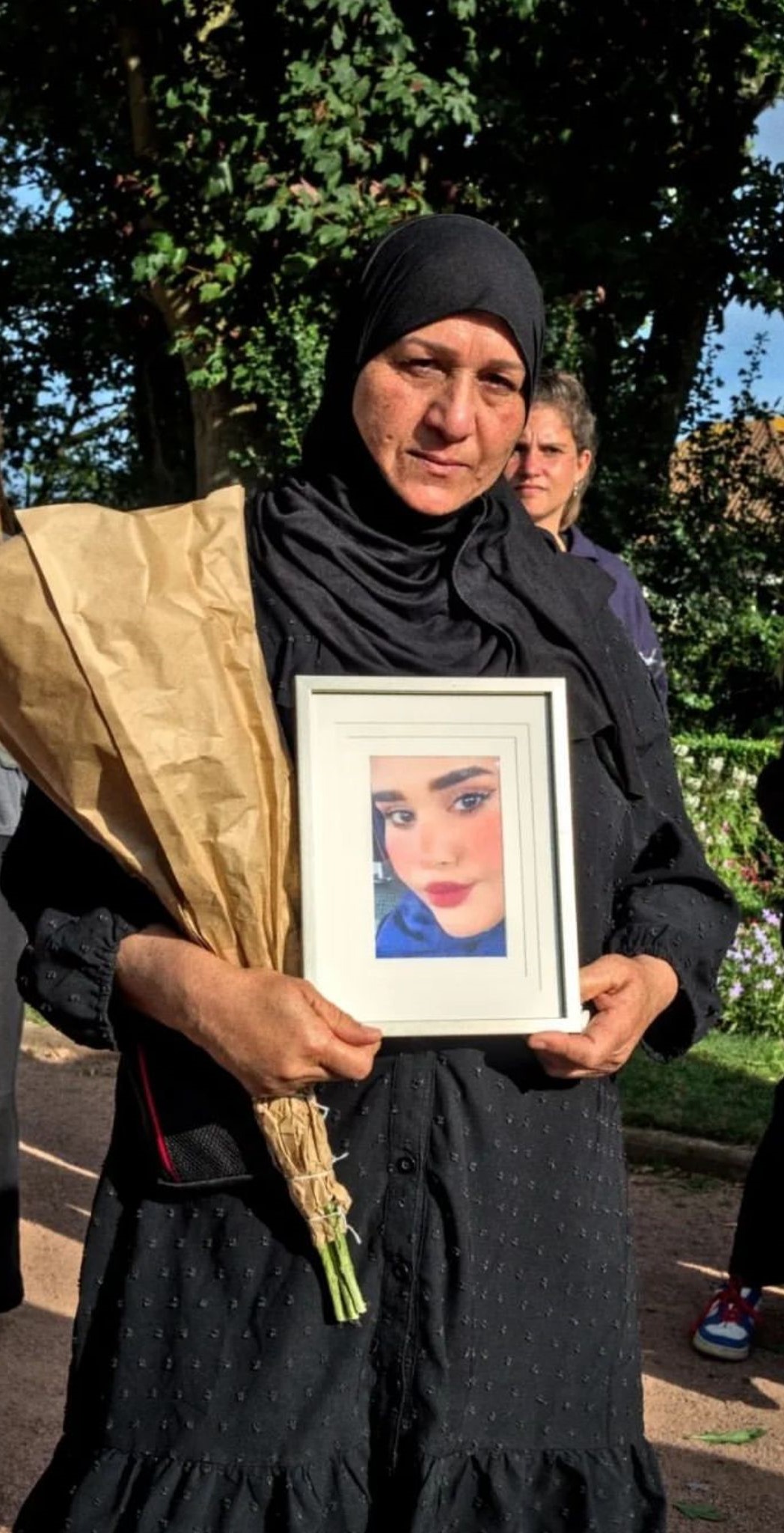 A woman in black with a black head scarf holds a picture of a young woman