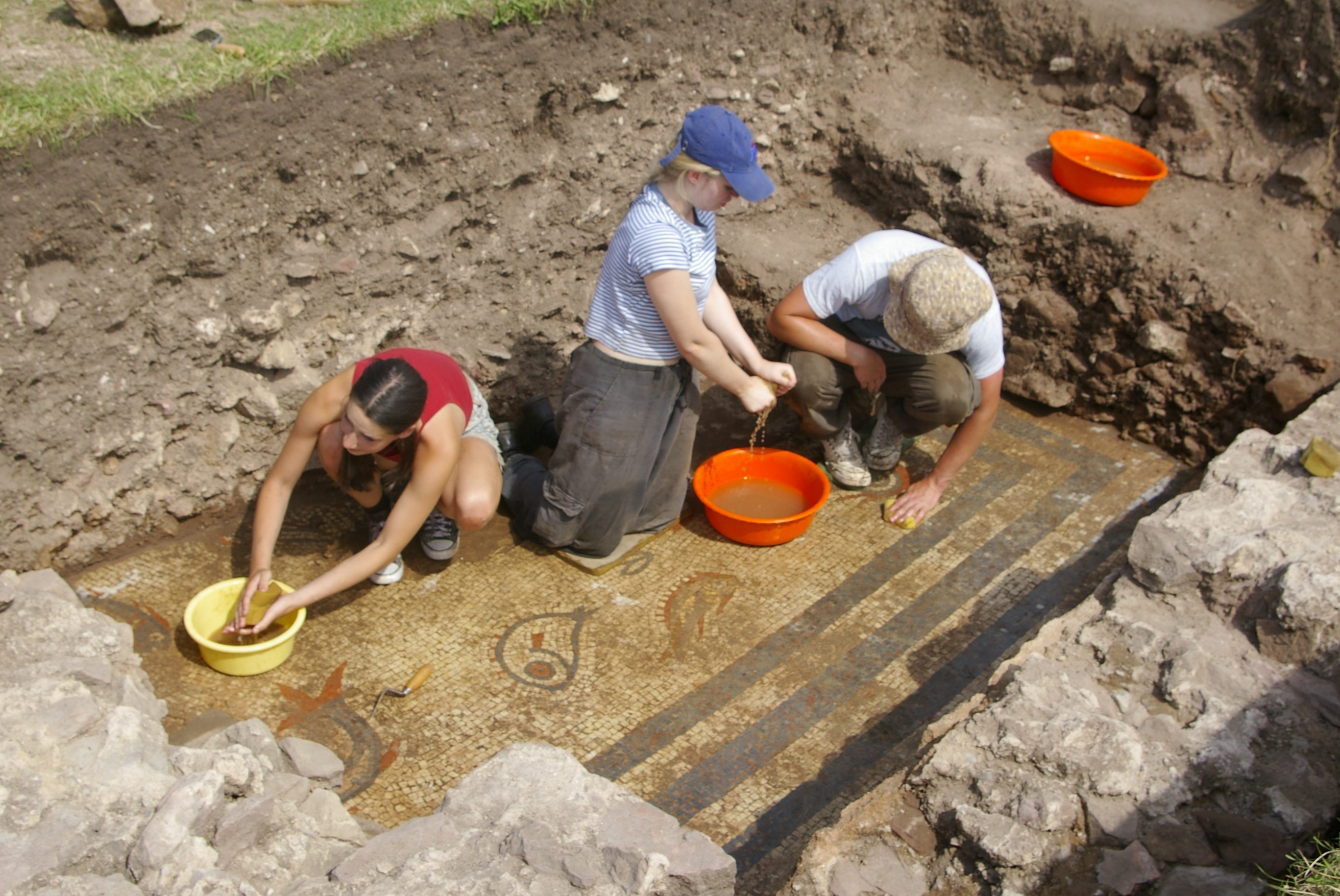 Three people in a trench cleaning the mosaic by hand