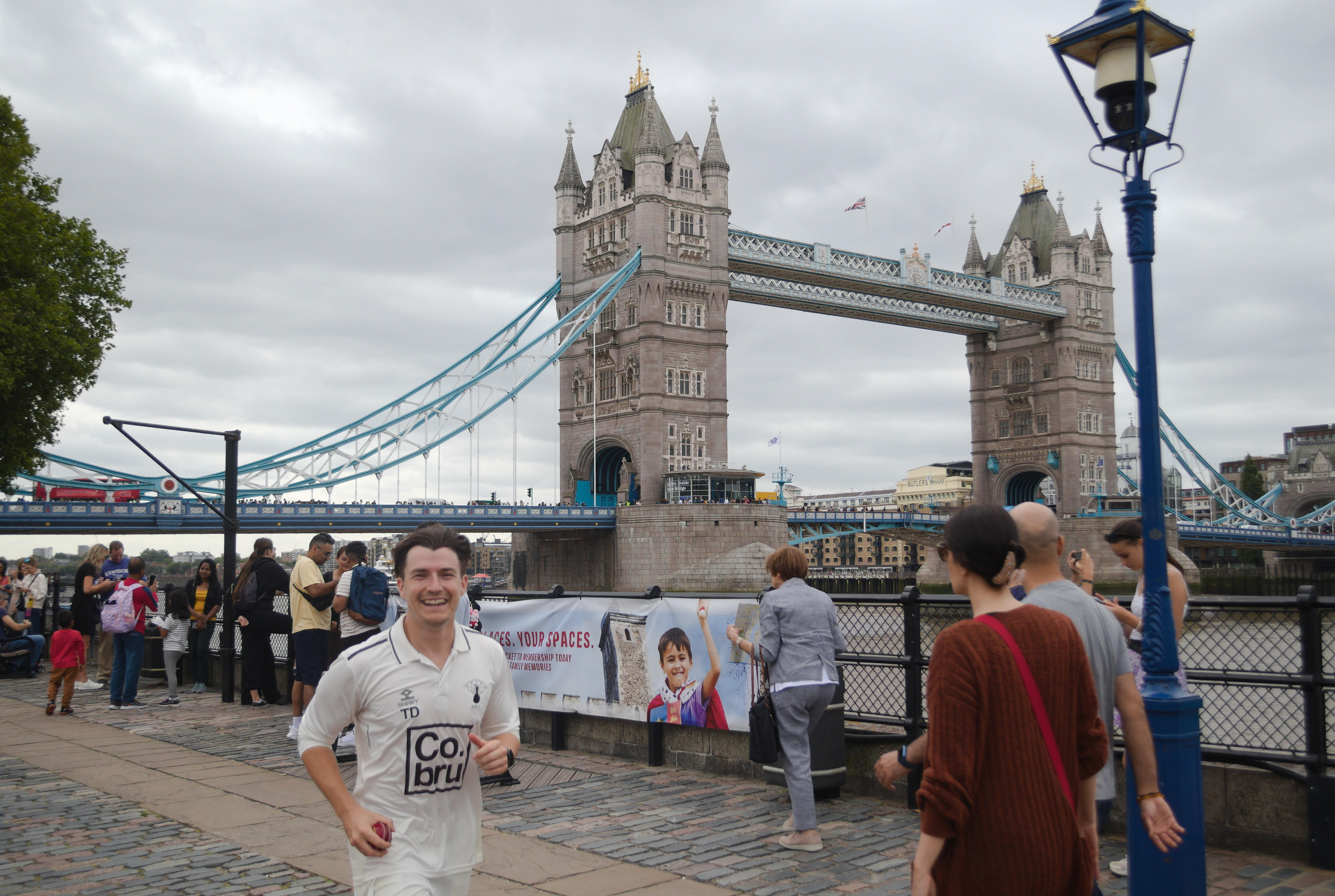 Man in full white cricket gear running past Tower Bridge