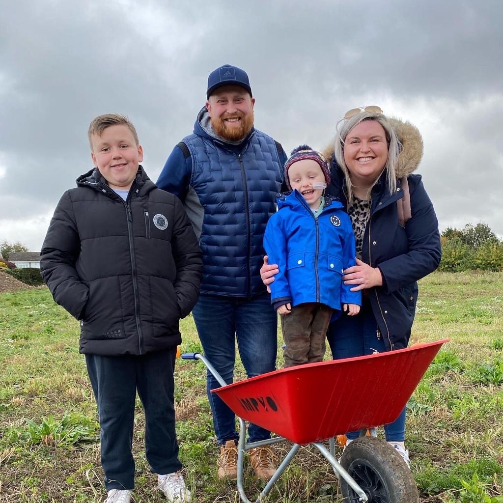 A couple and their two sons, one of whom is standing in a red wheelbarrow