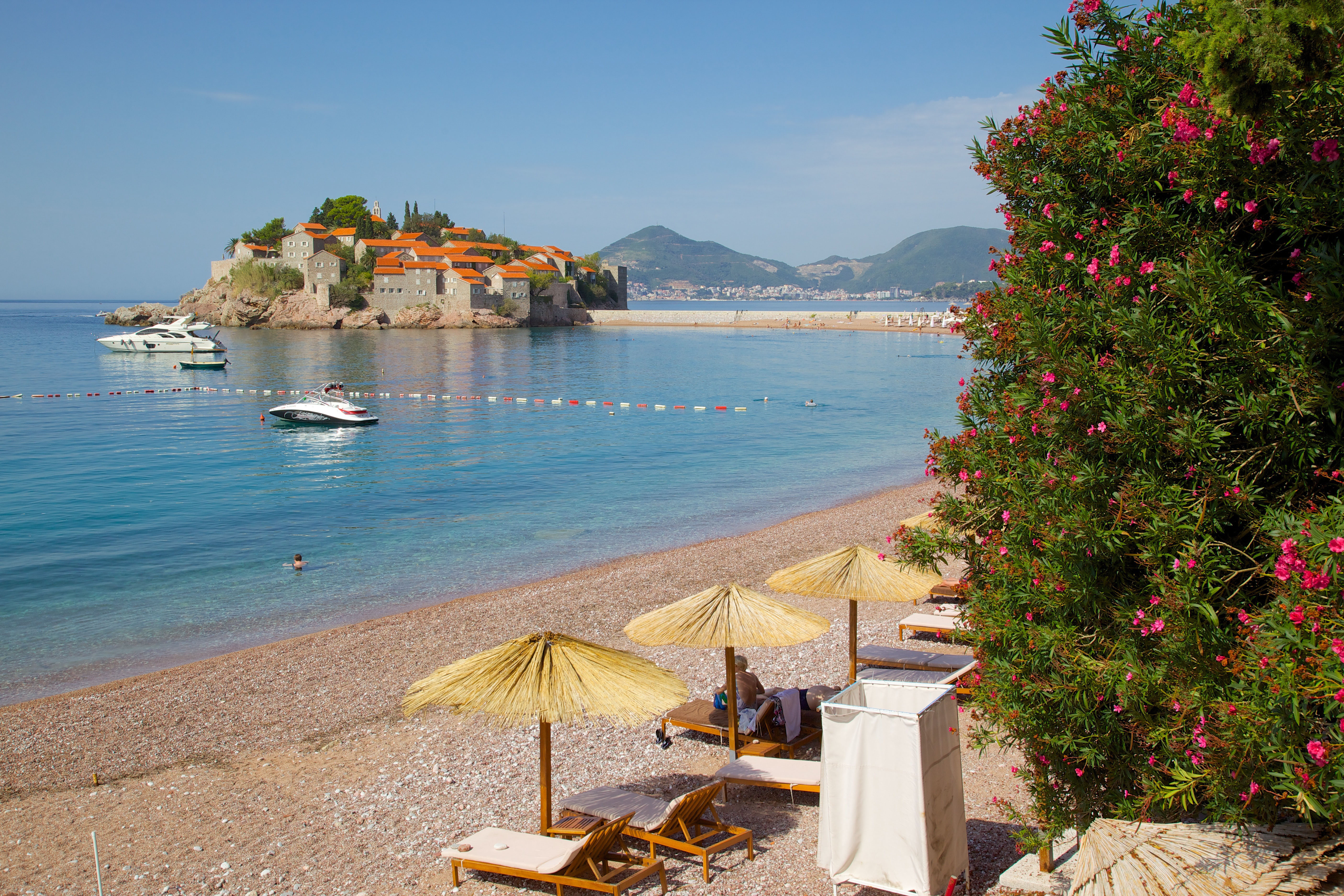 Straw umbrellas and sun loungers on pebbly Budva Bay with a picturesque view of The Budva Riviera in Montenegro