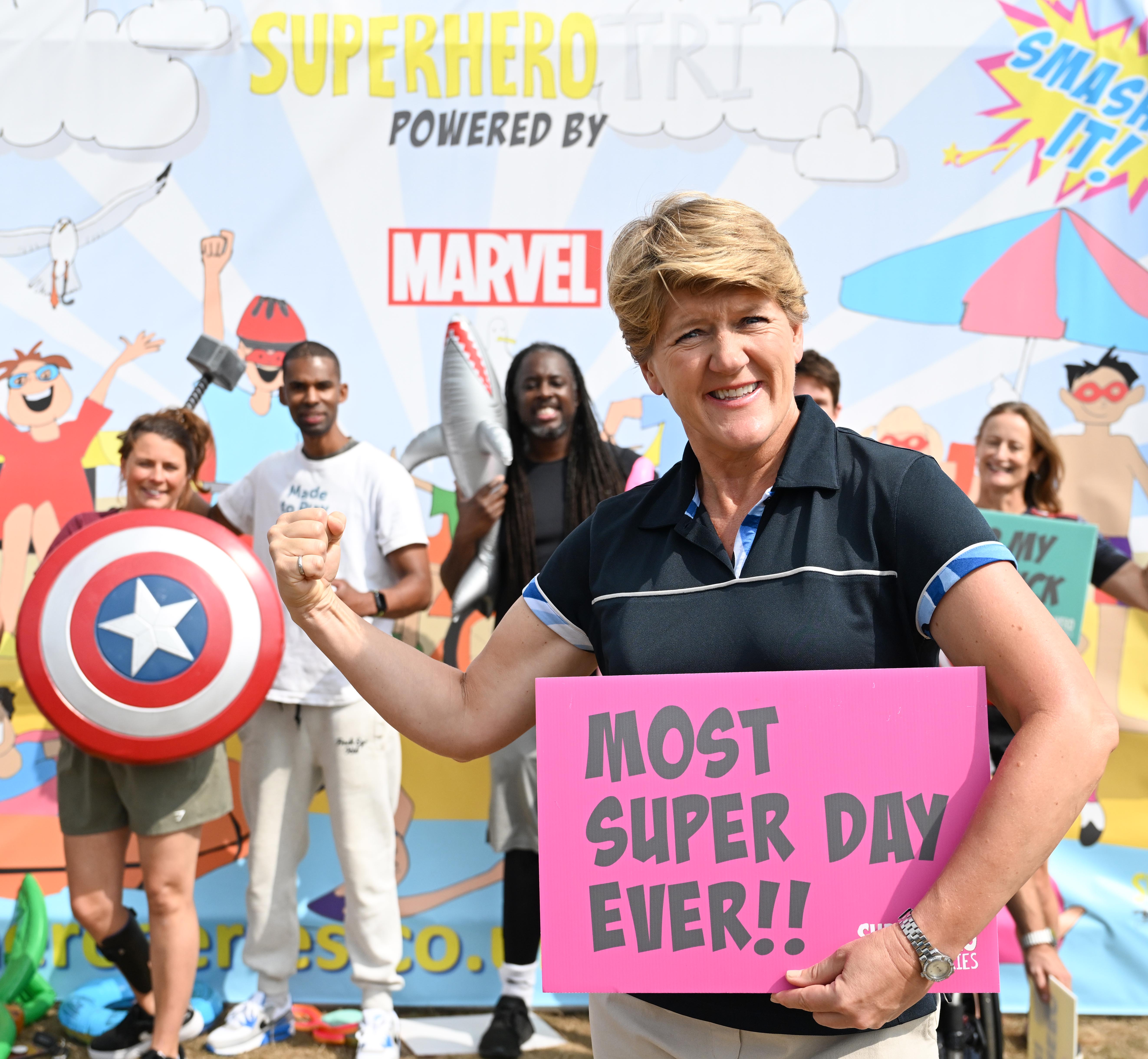 Clare Balding posing with a sign and looking at the camera