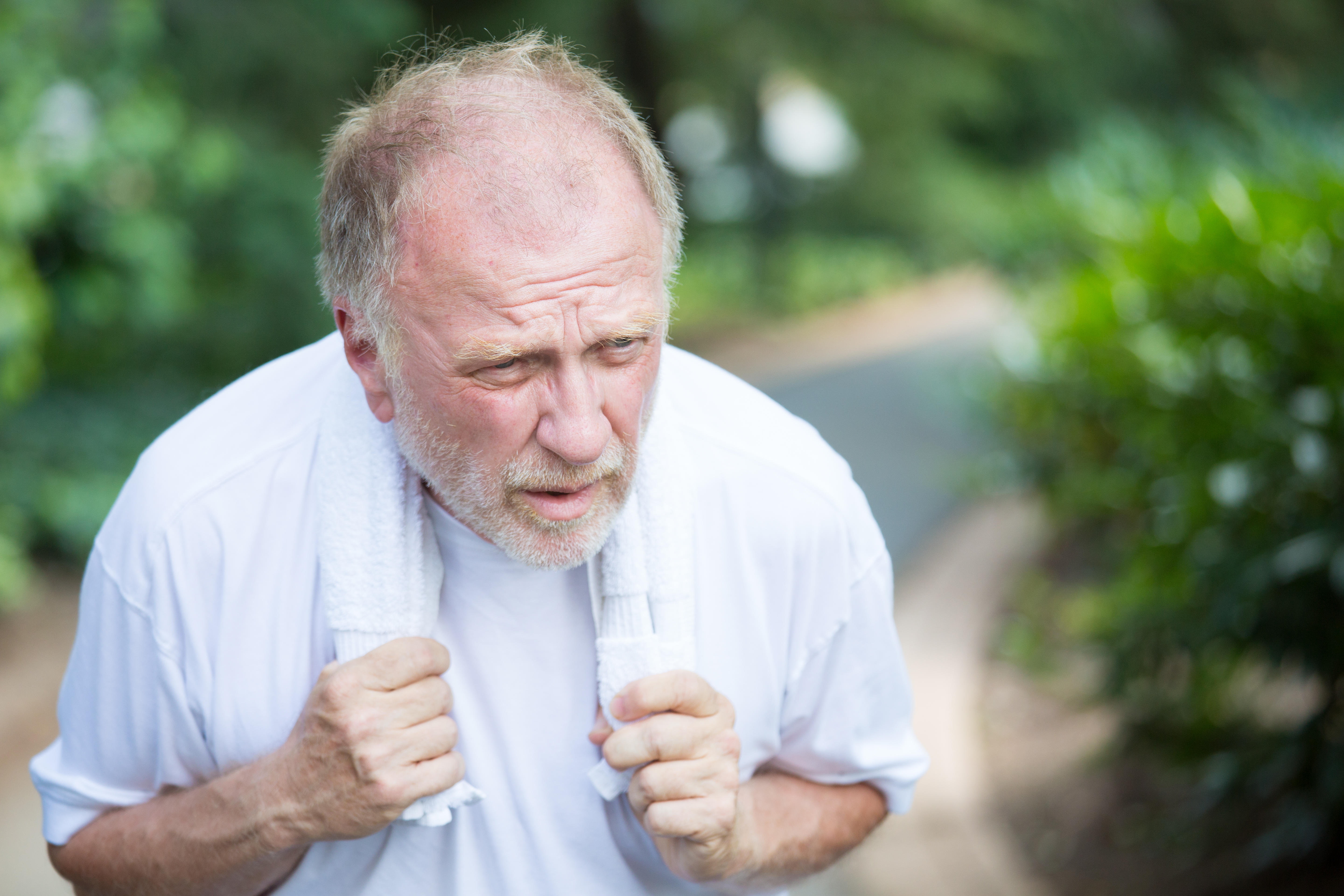 Senior man wheezing while holding a towel around his neck after a run