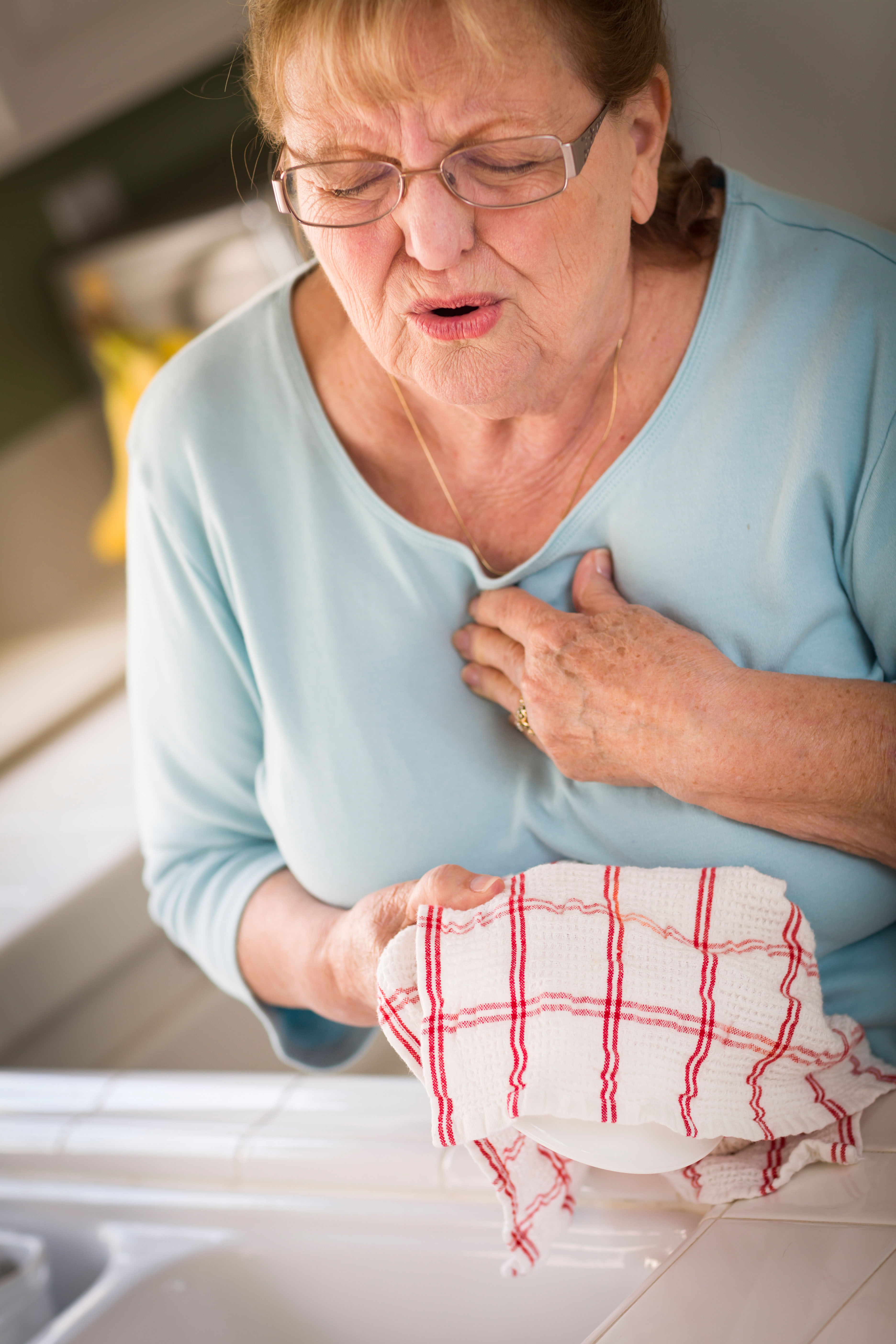 Senior woman clutching at her chest while washing up due to severe chest pains