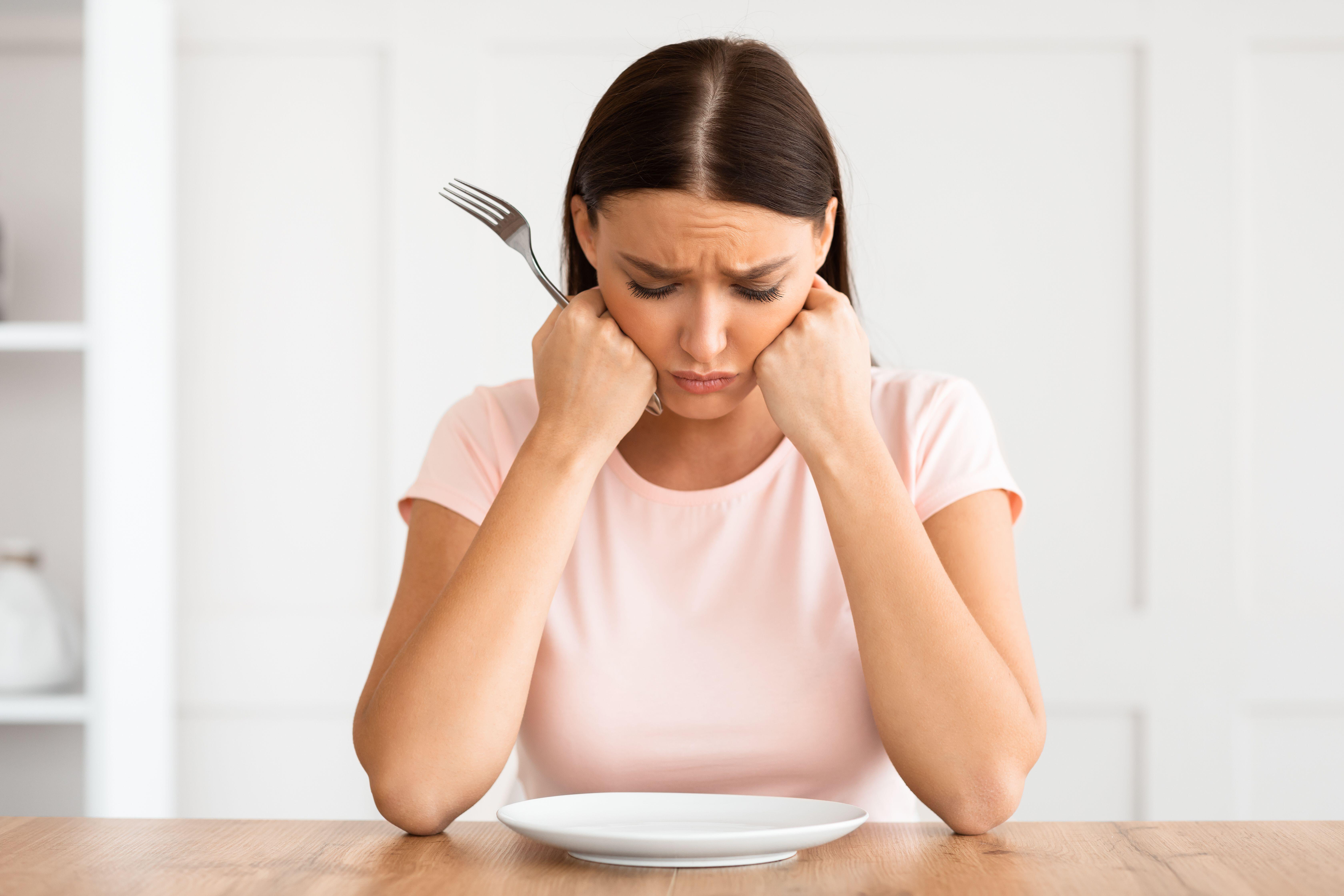 Unhappy woman sitting at a table staring at an empty plate in front of her