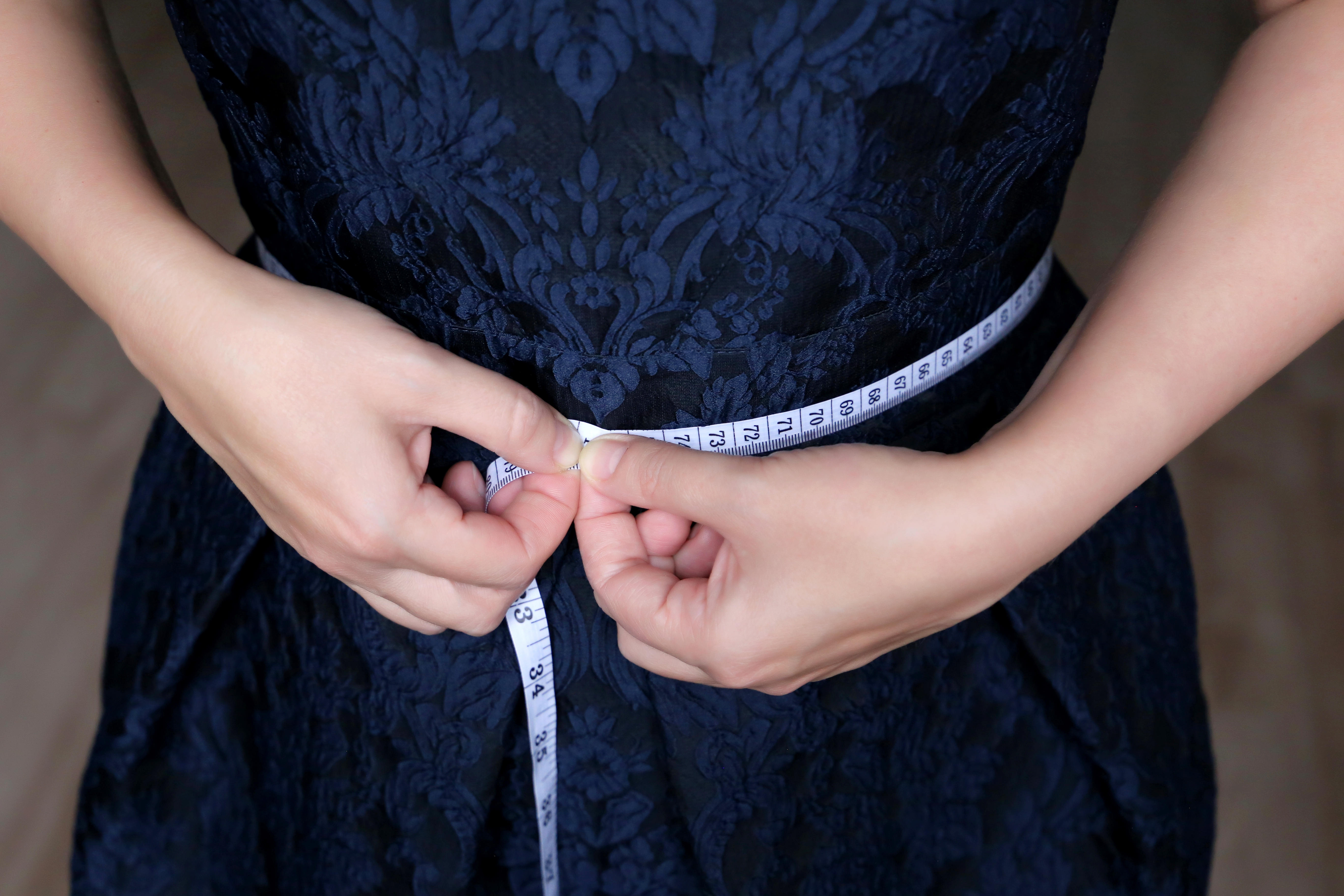 A girl wearing a blue dress standing with measuring tape around her waist