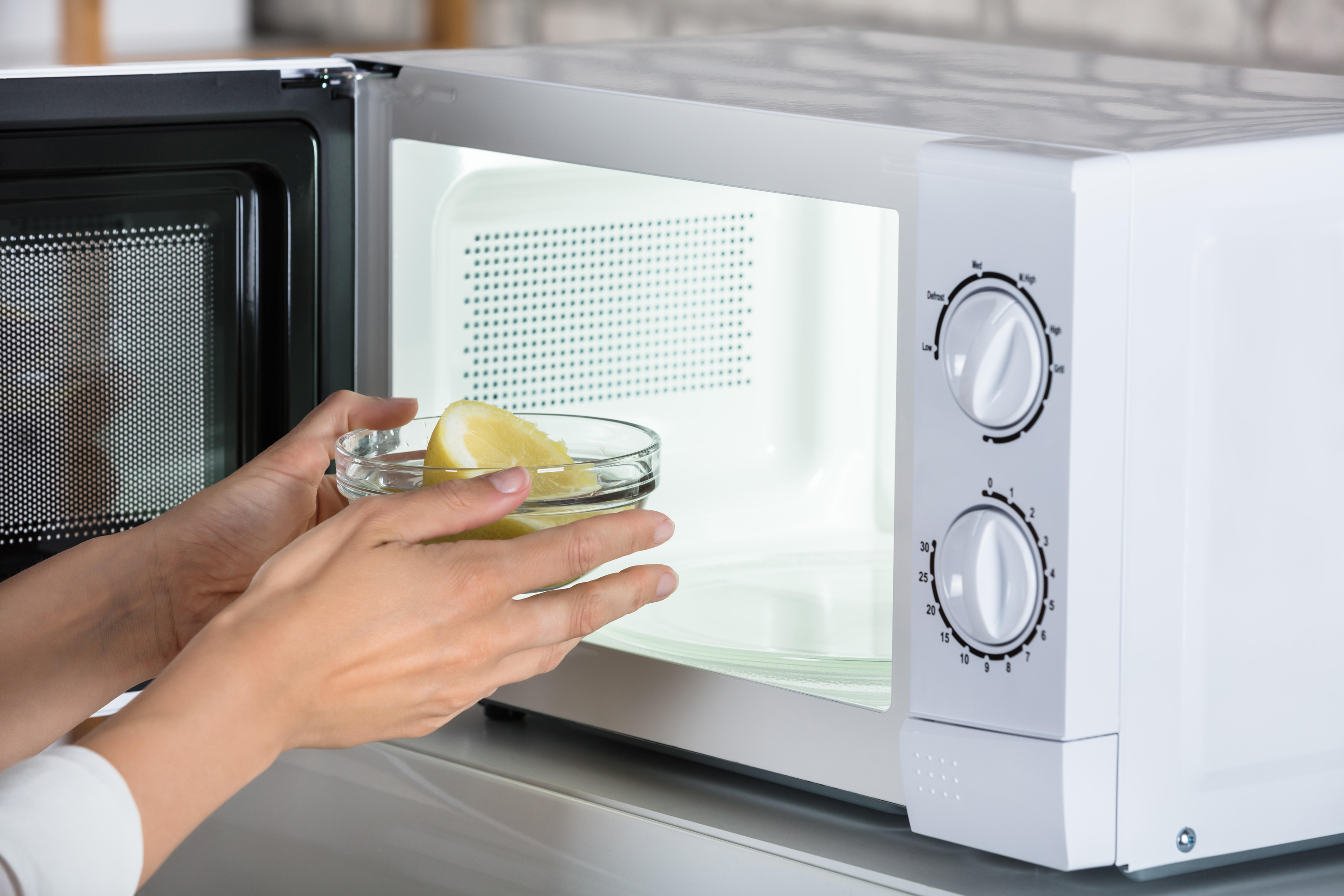 Woman putting bowl of sliced lemon in microwave 