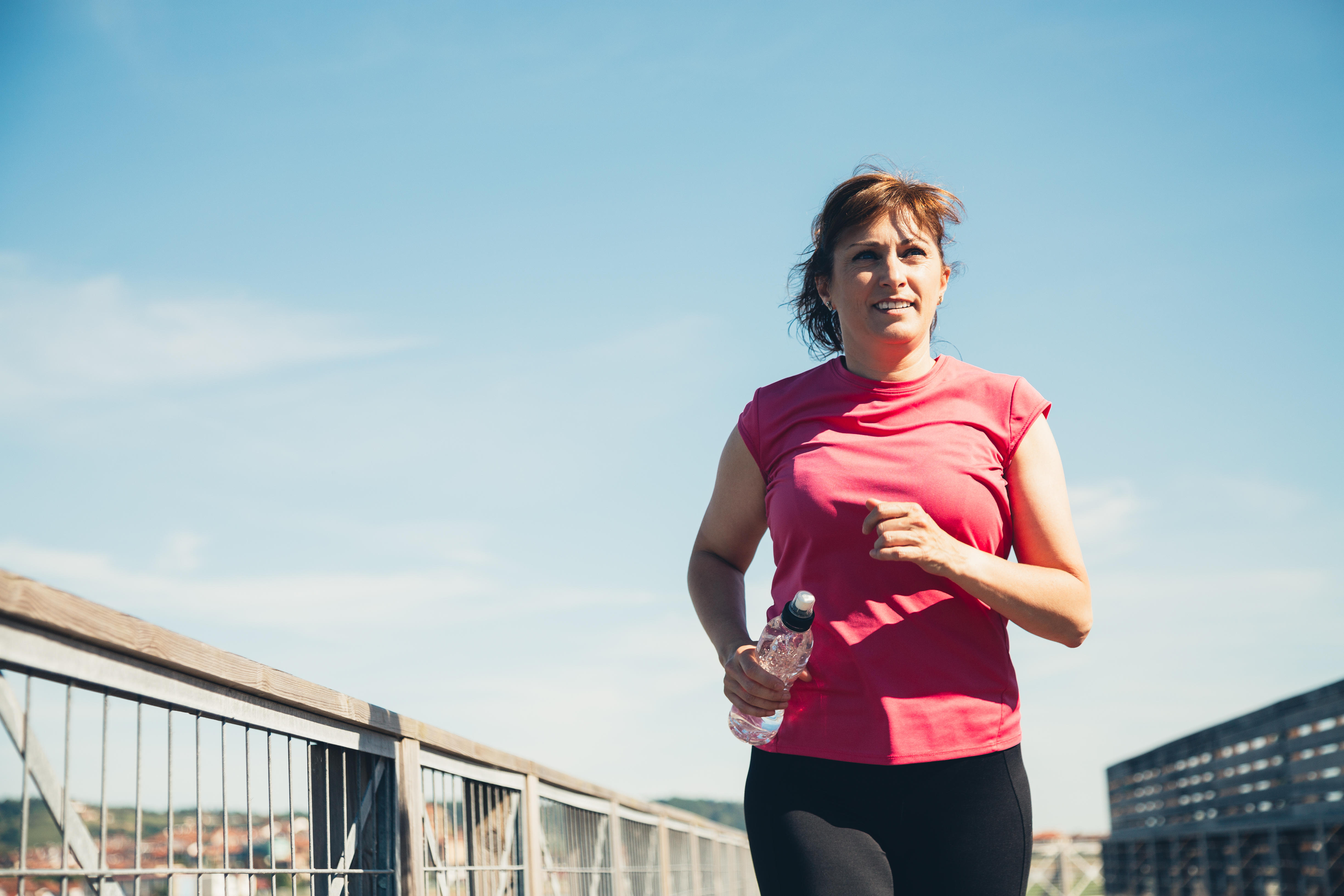 Middle aged woman running with a water bottle in hand on a sunny day