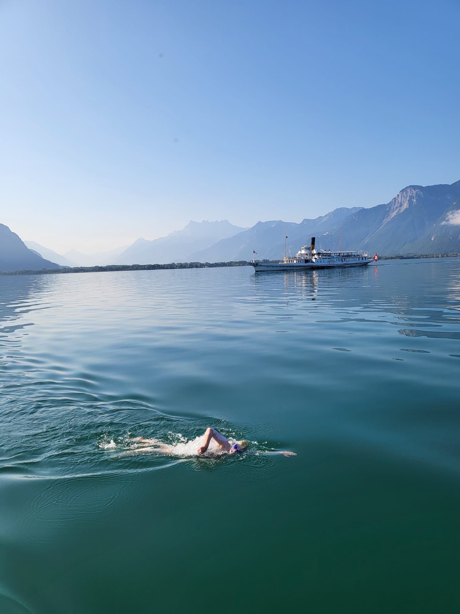 Sam Farrow swimming, with a boat and mountains in the background