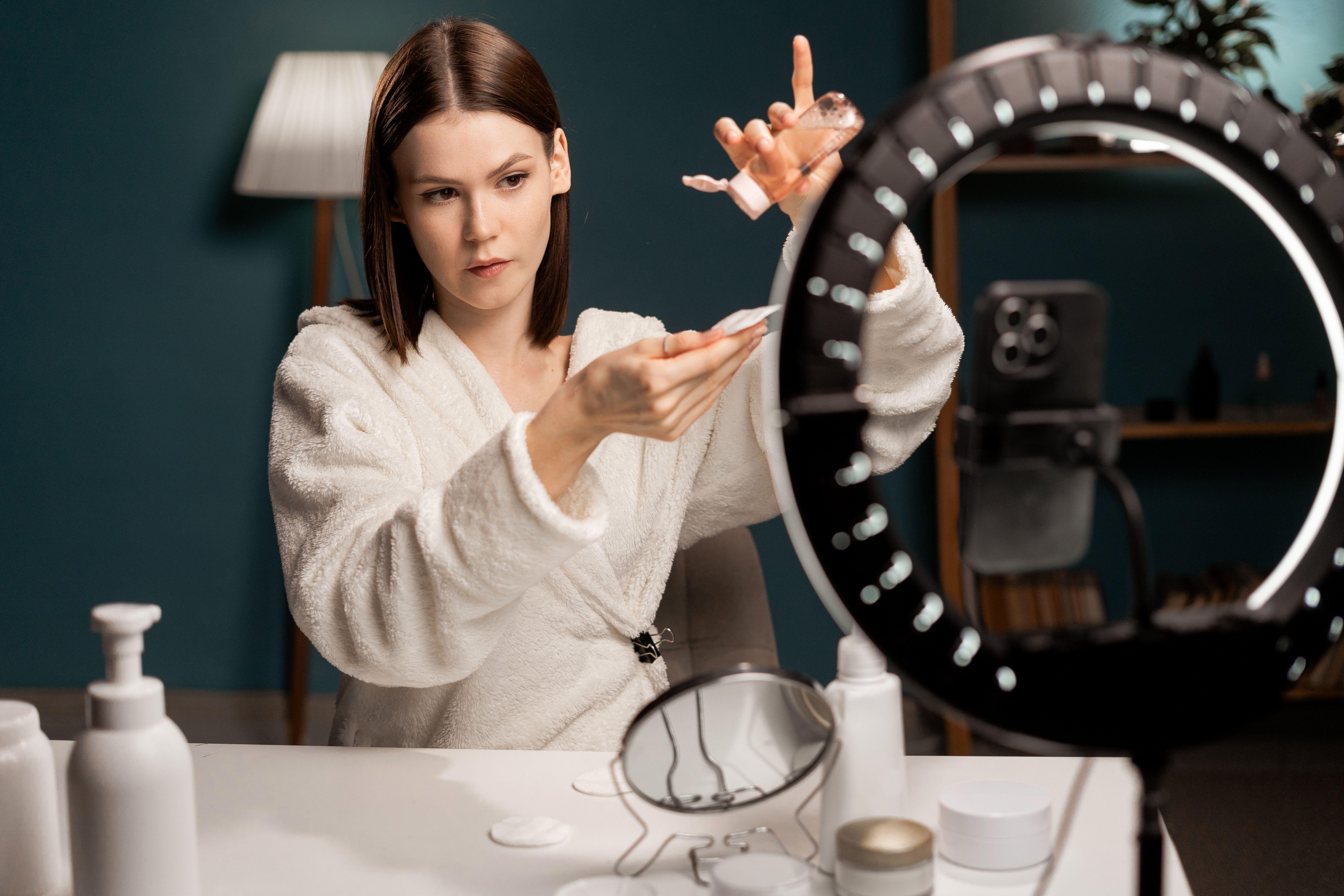 Young woman applies skincare in front of ring light and smart phone 