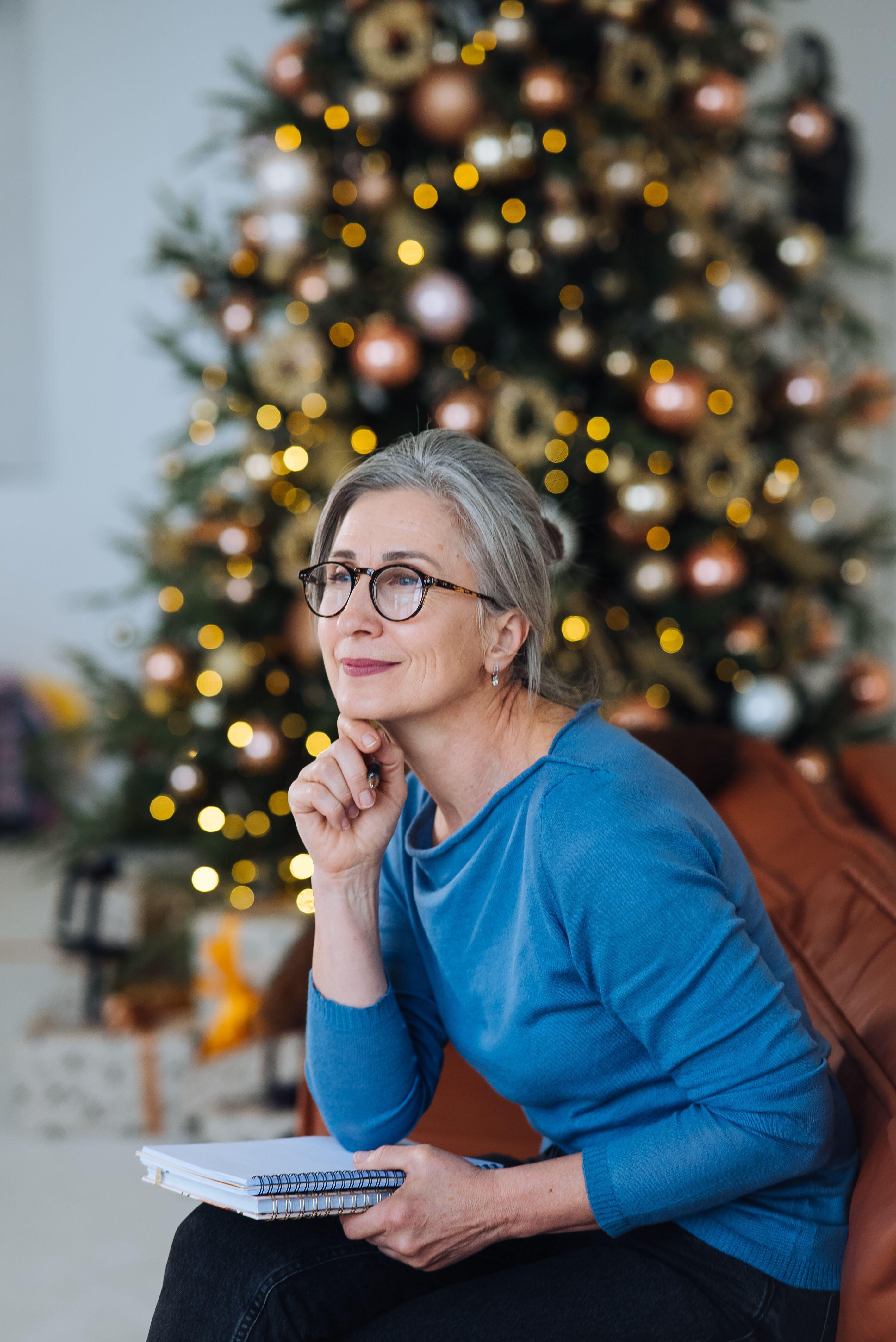 Happy senior woman in glasses thinking and writing a diary at home