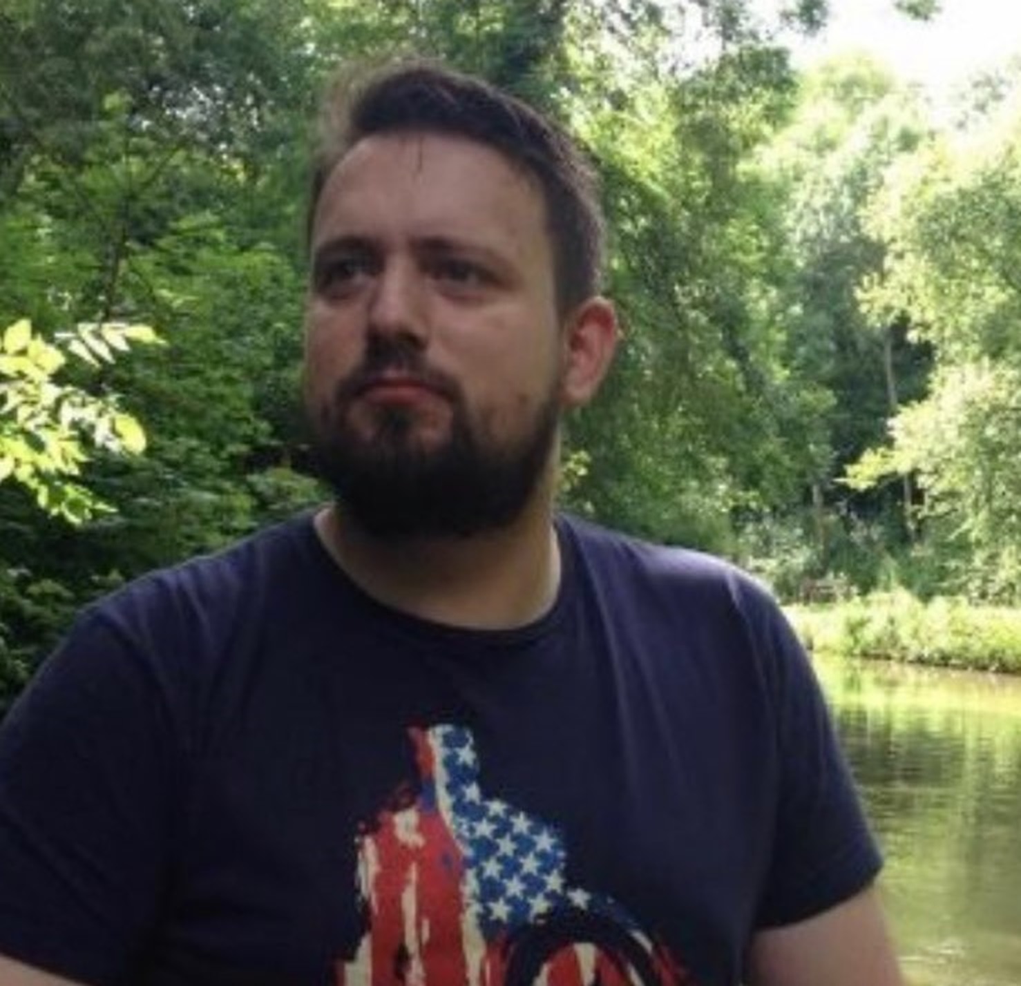 James Binks in a T-shirt with water and trees in the background