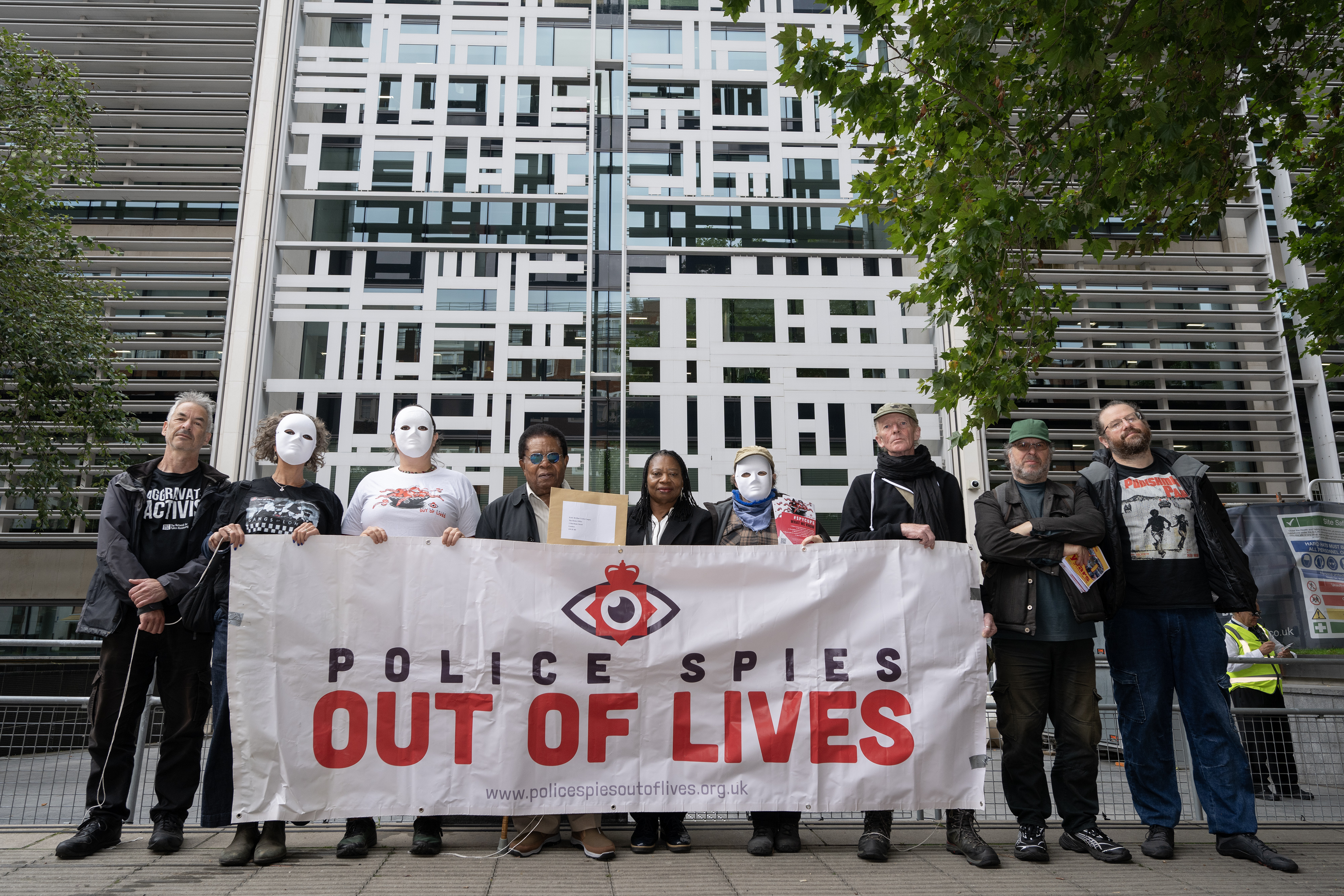 Campaigners, some in masks, holding a banner reading Police Spies Out Of Our Lives outside the Home Office