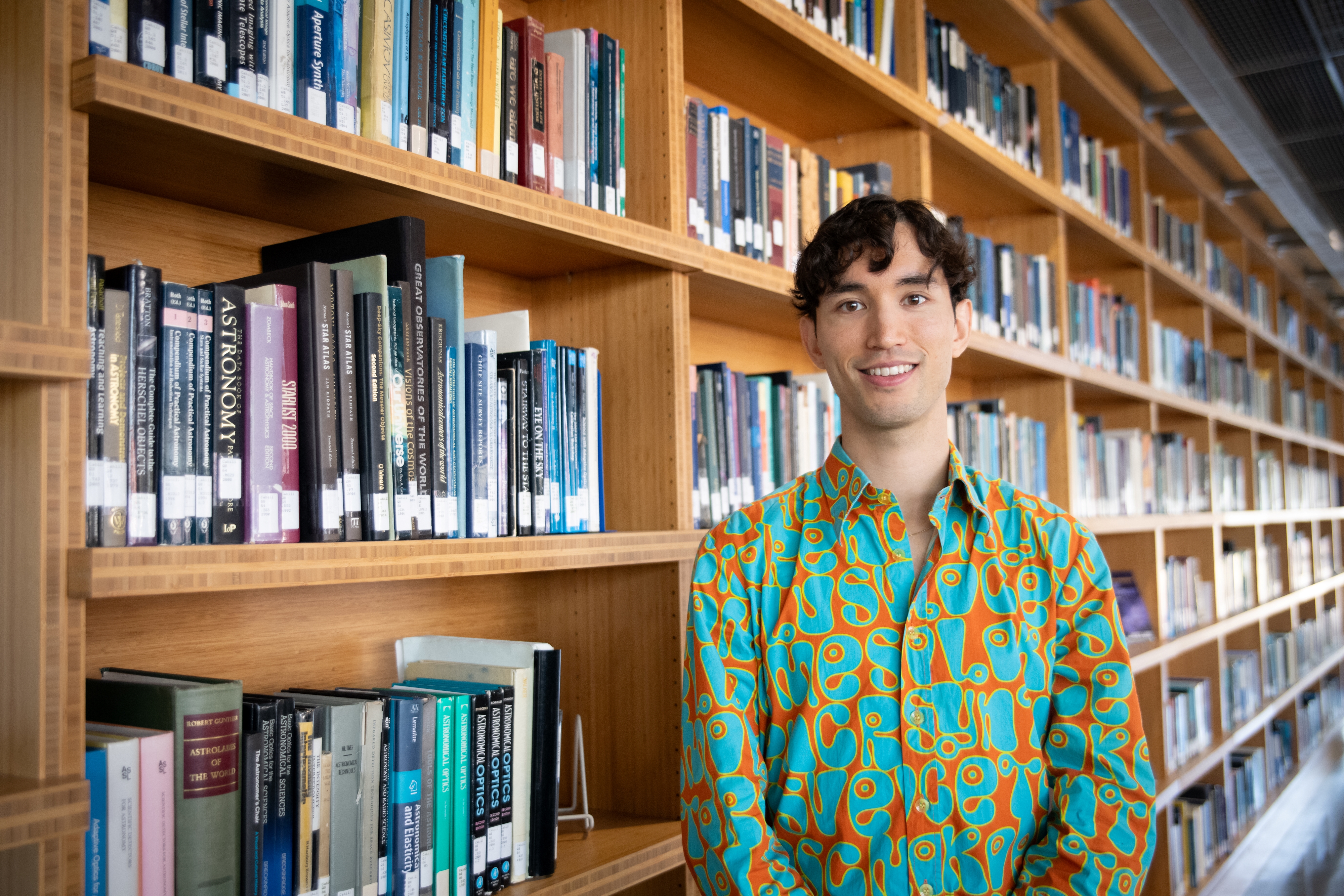 Martijn Oei smiling, standing in a library and wearing a vibrant-coloured shirt