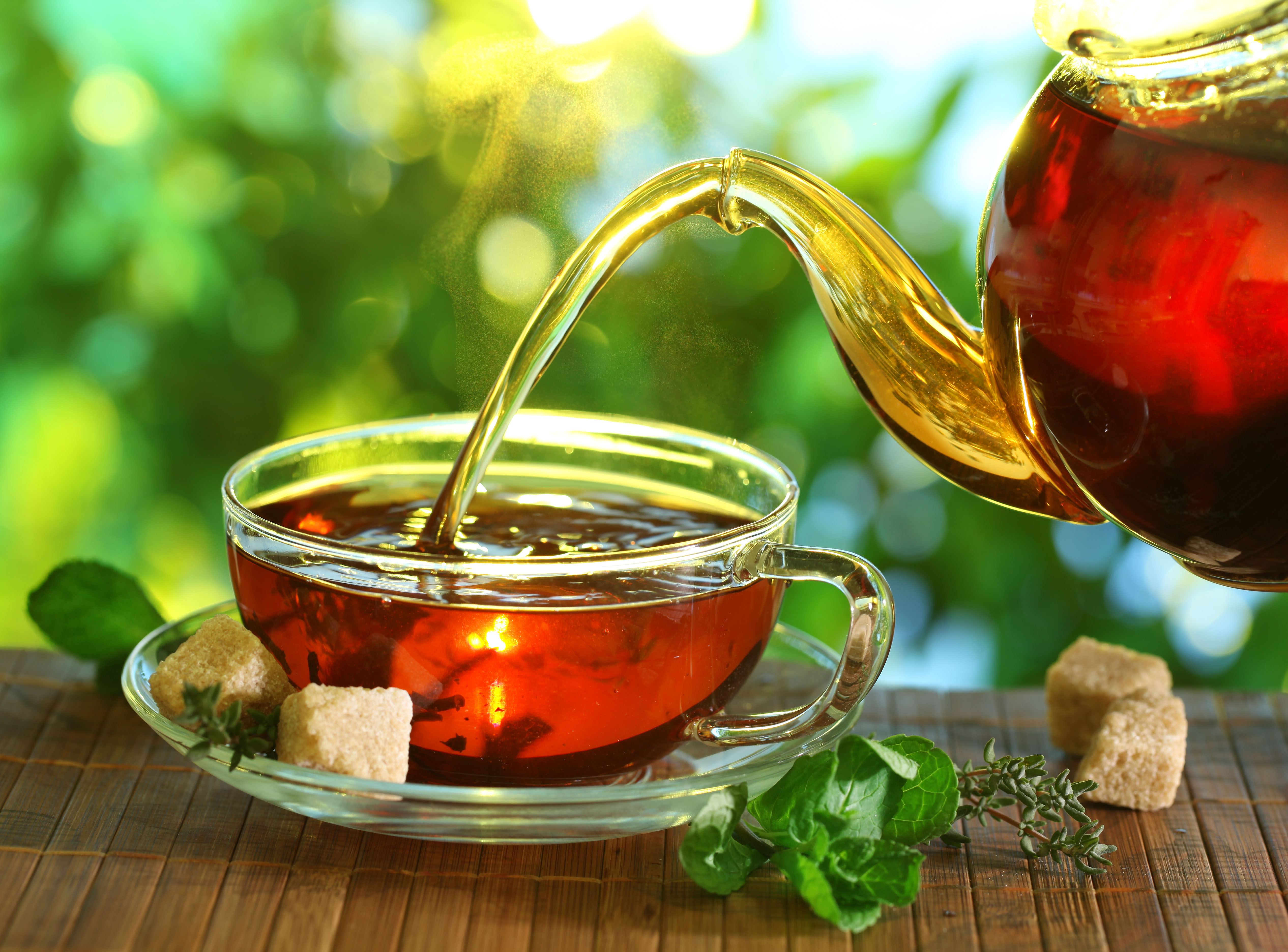 Someone pouring tea from a glass teapot into a glass cup 