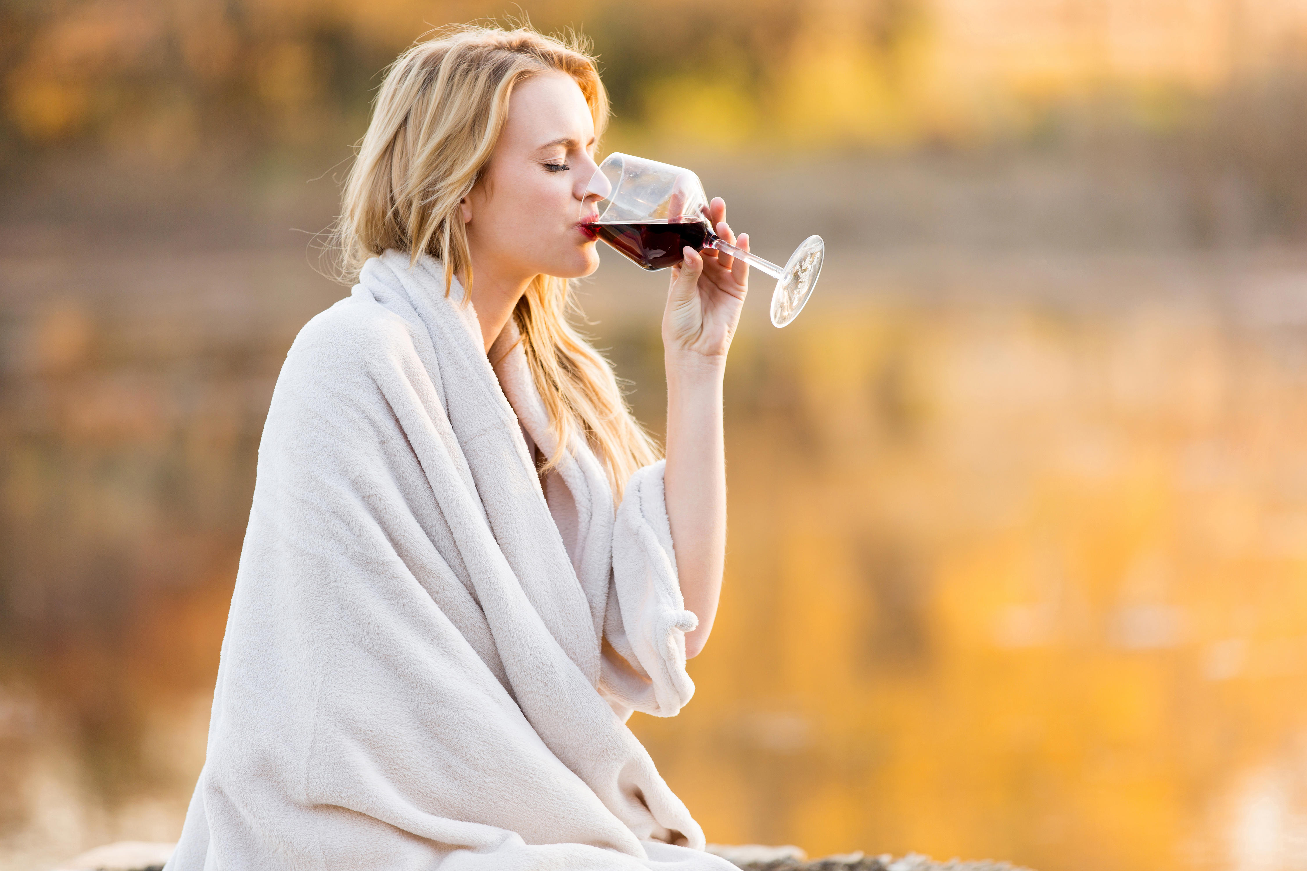 Blonde woman wrapped in a blanket drinking red wine