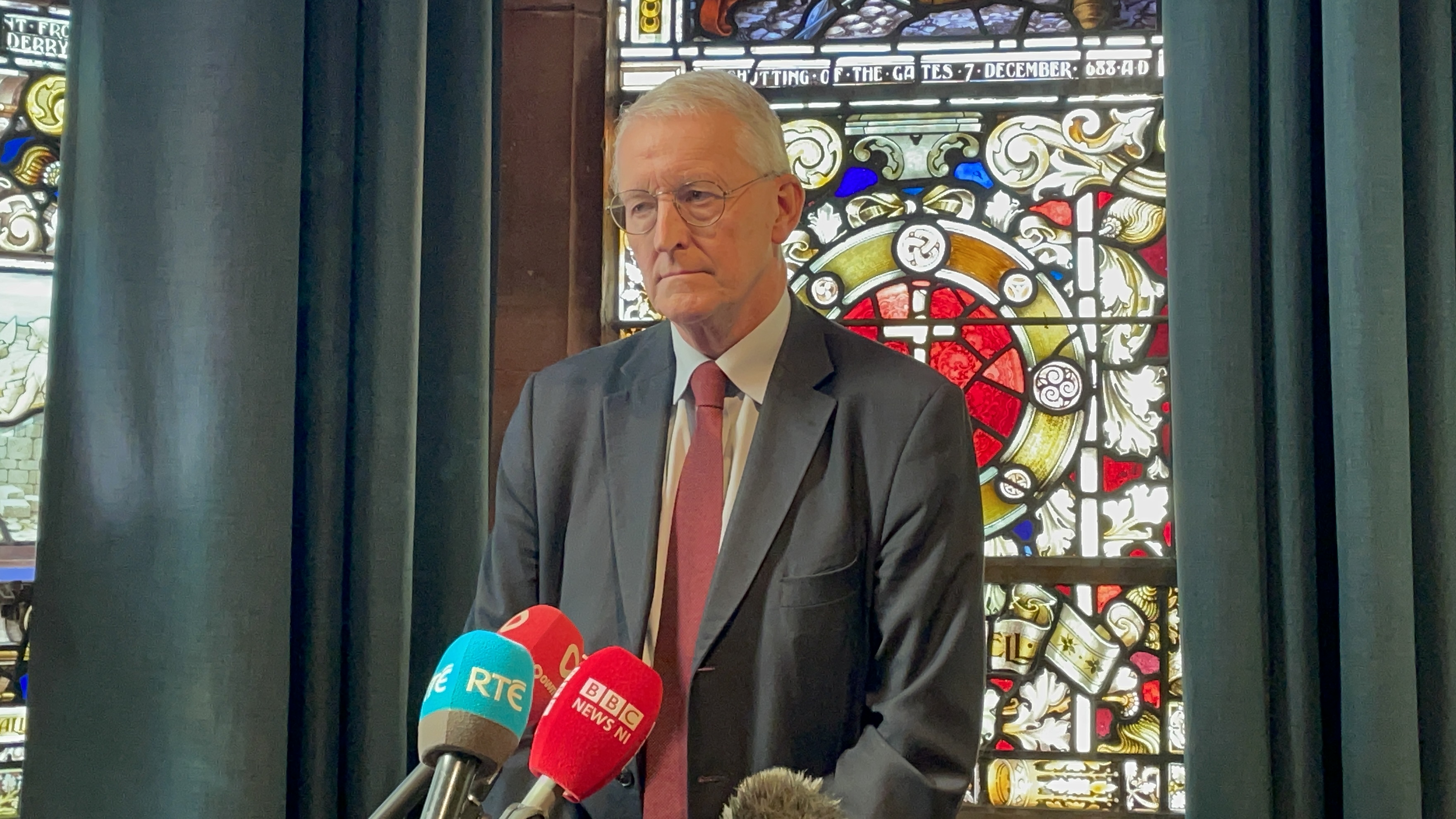 Man in a grey suit in front of a stained glass window