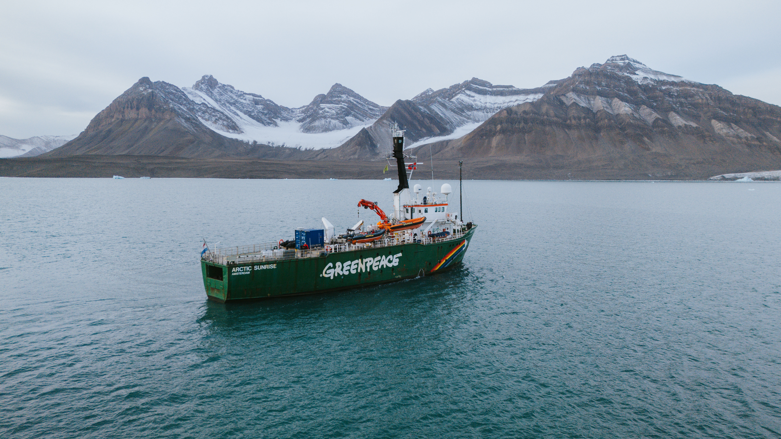 Greenpeace vessel Arctic Sunrise sailing through Norwegian Sea with mountains behind