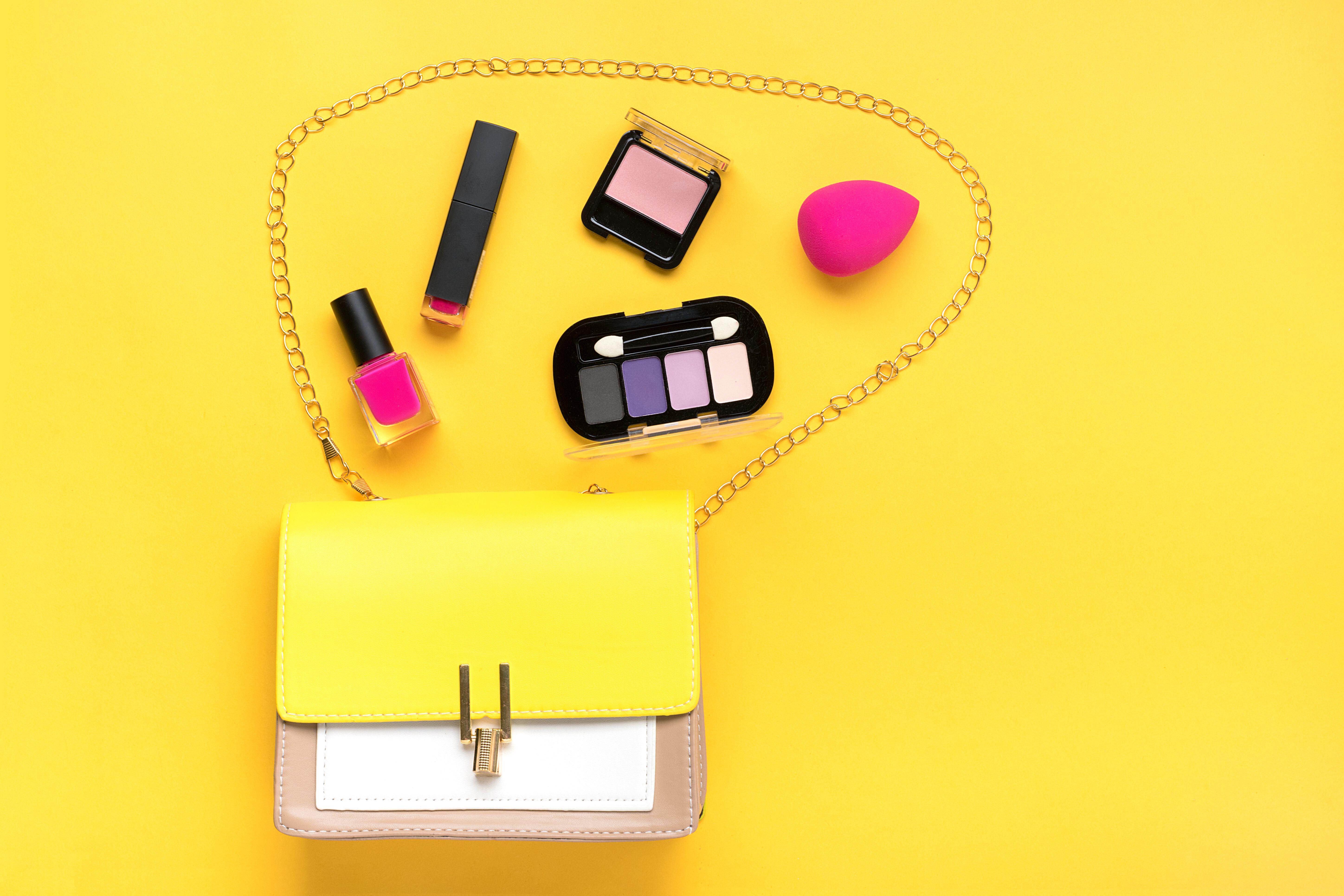 Makeup coming out of hand bag on yellow flat lay