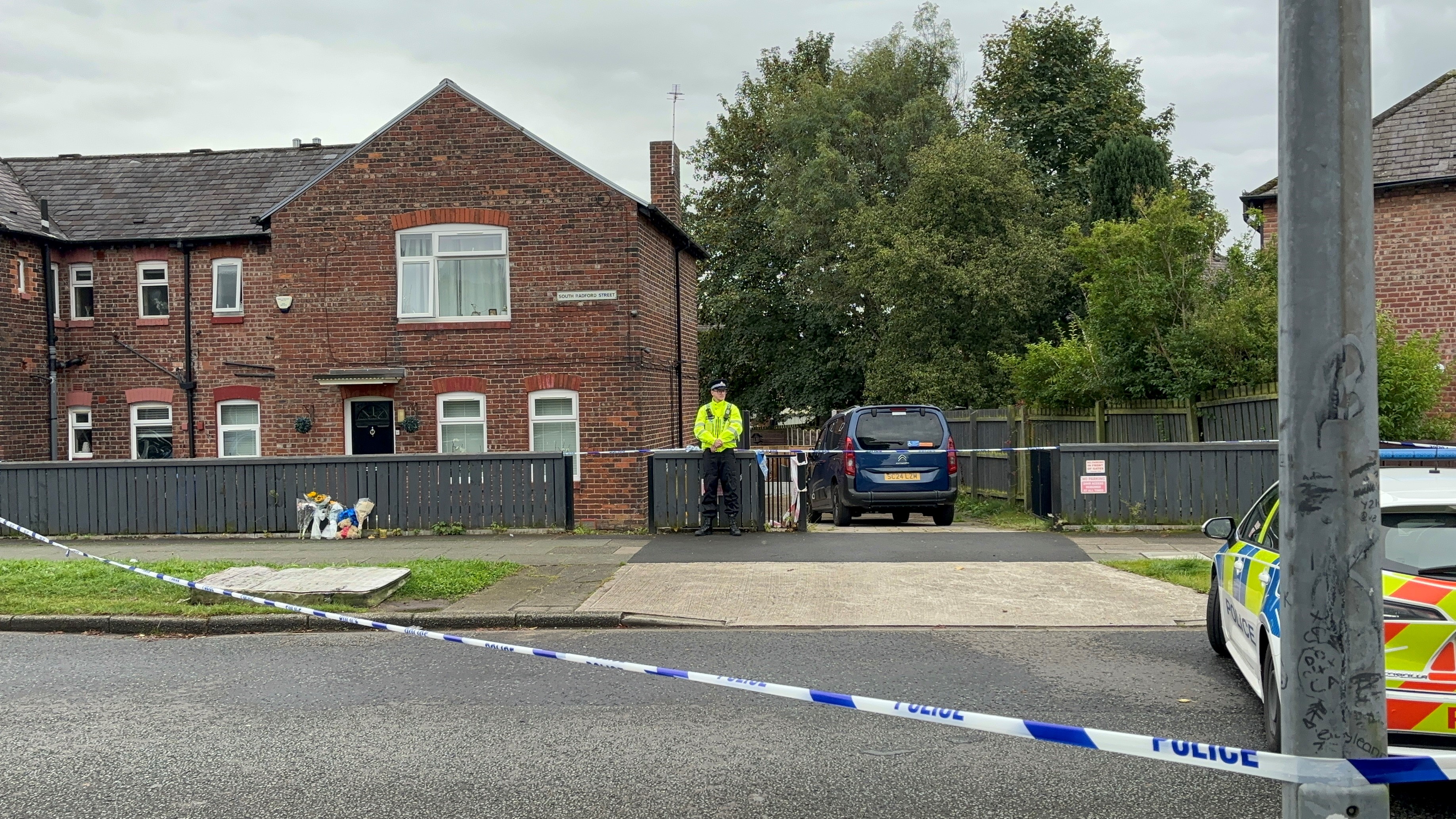 Police officer, police tape and flowers outside a house