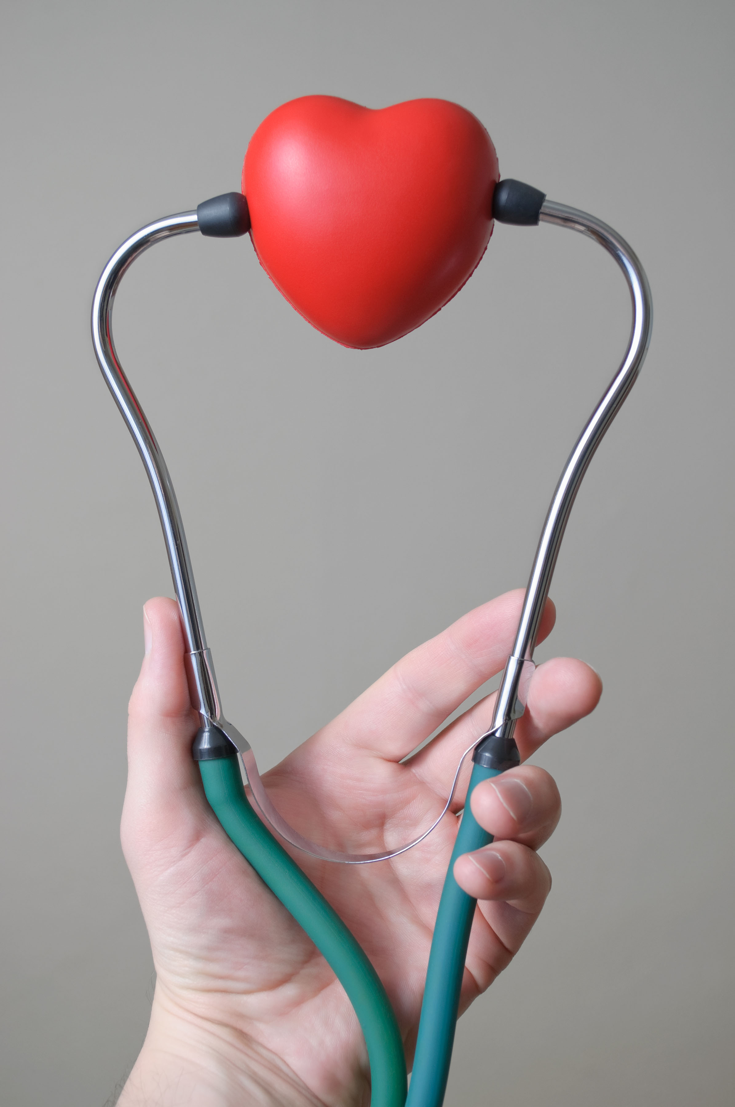 Man's hand holding a red heart shape and stethoscope