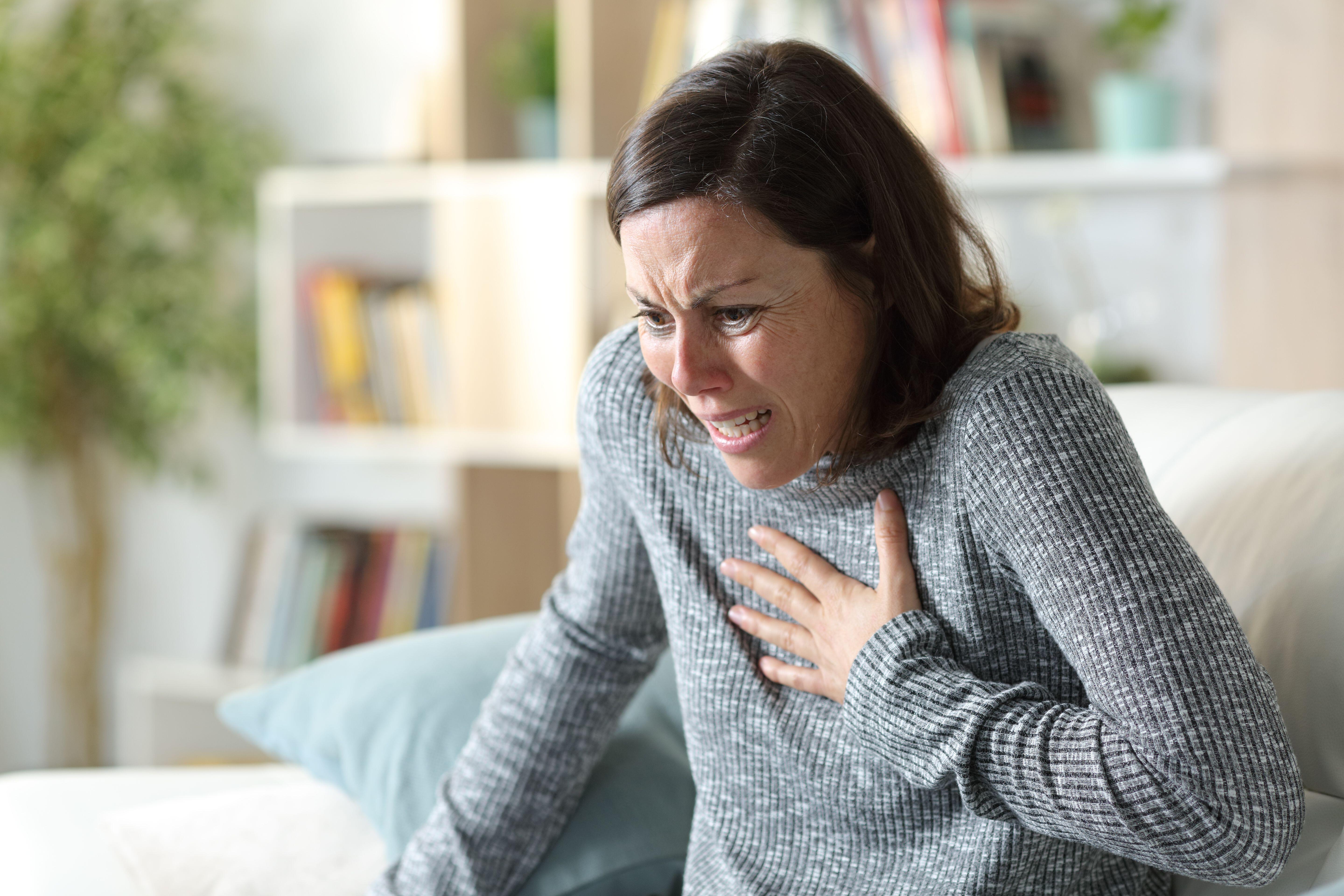 Scared woman sat on a sofa clutching her chest as she suffers from a heart attack