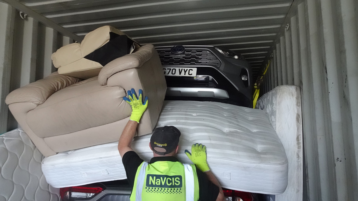 The front of a car can be seen high in a container with an armchair and a mattress placed in front of it.