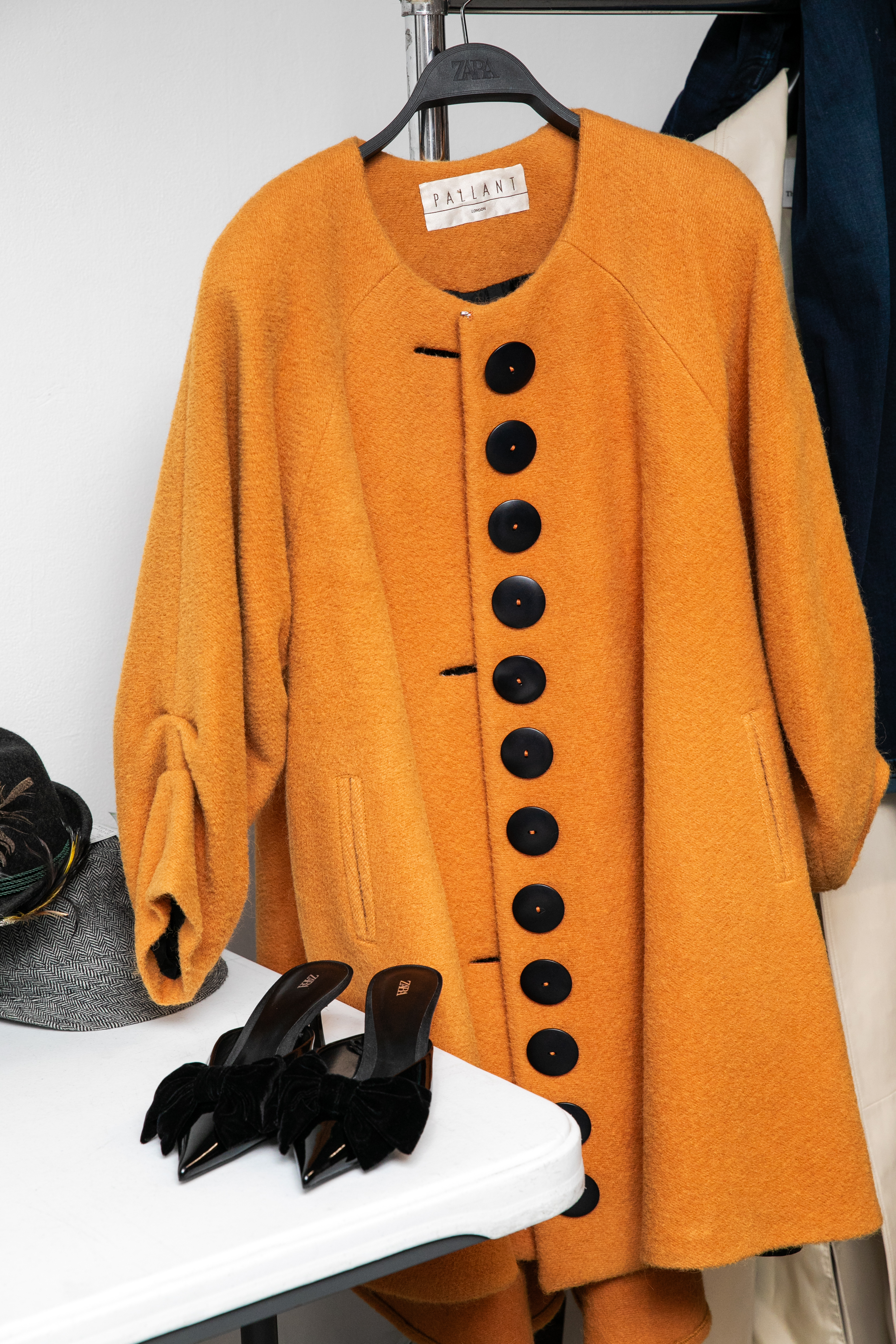 An orange Pallant coat on a hanger and black shoes